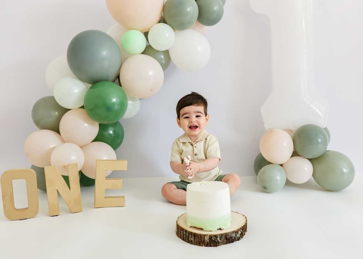 Minimalist cake smash photo with mint green cake, wood slice, and eucalyptus balloon garland.