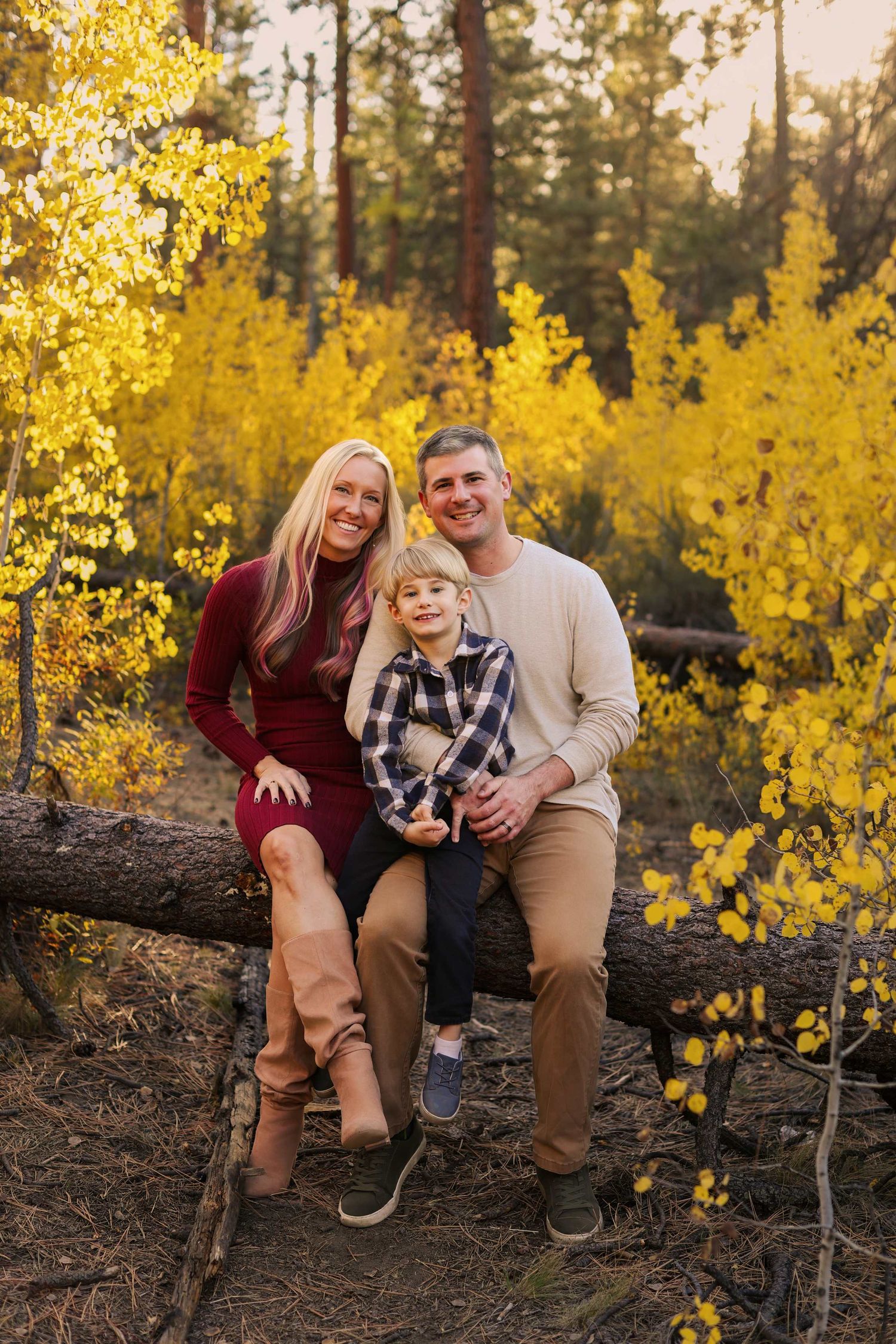Family of three smiling outdoors on a log surrounded by vibrant yellow autumn foliage in a forest setting. Shevlin Park Bend Oregon