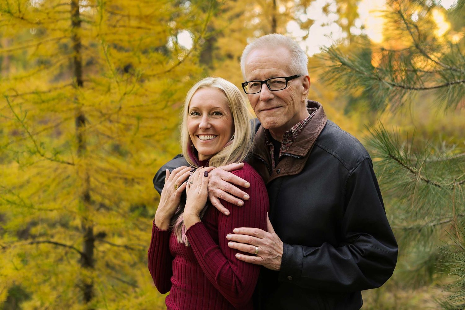Loving couple embraces outdoors with golden fall colors in background.