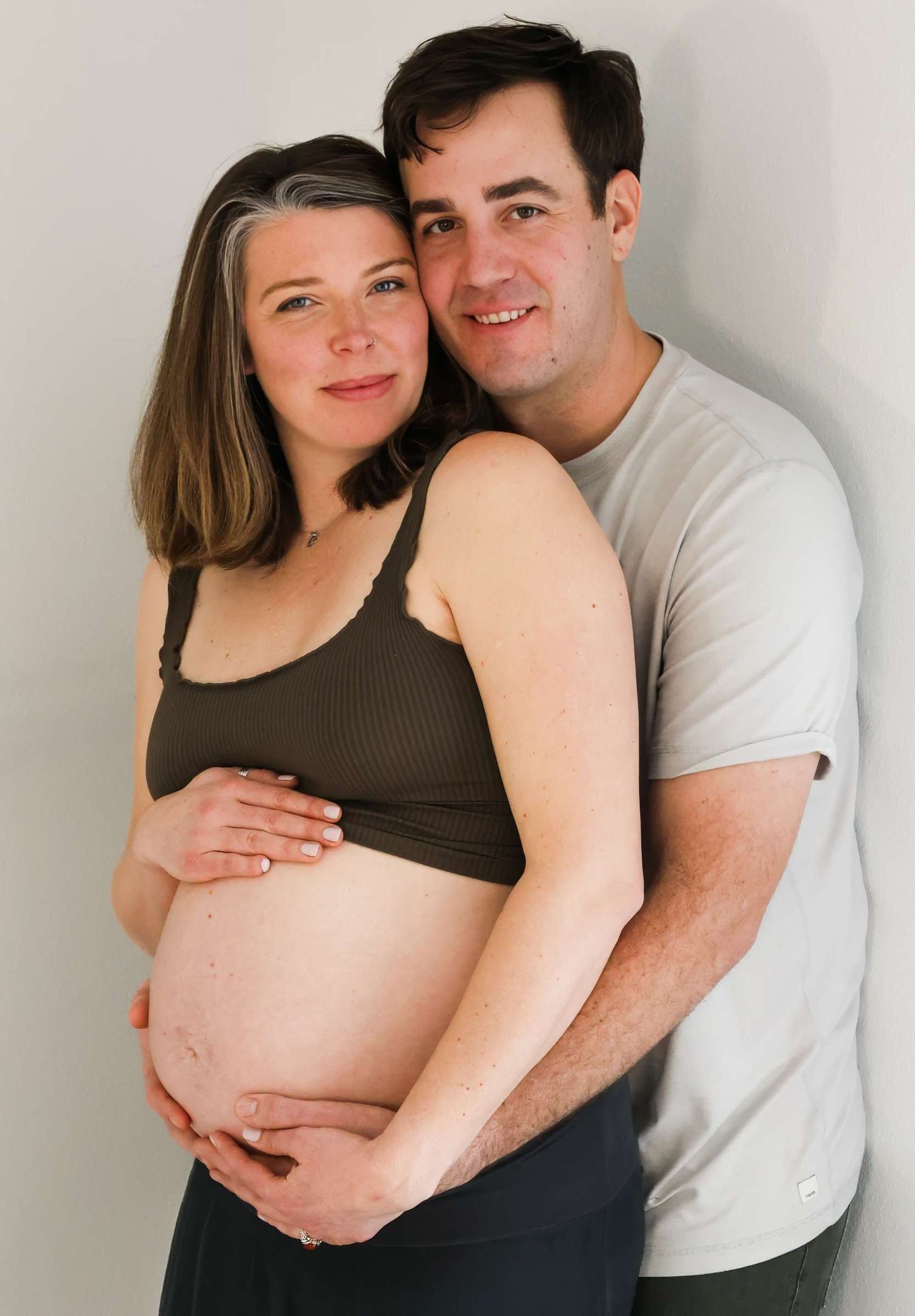 A series of intimate maternity photos showing a couple embracing against a white wall in black and white tones. Redmond Oregon Studio