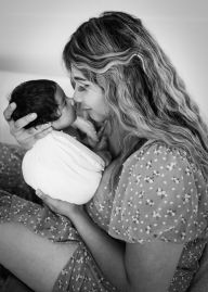 A tender black and white portrait showing a gentle moment between parent and newborn baby.