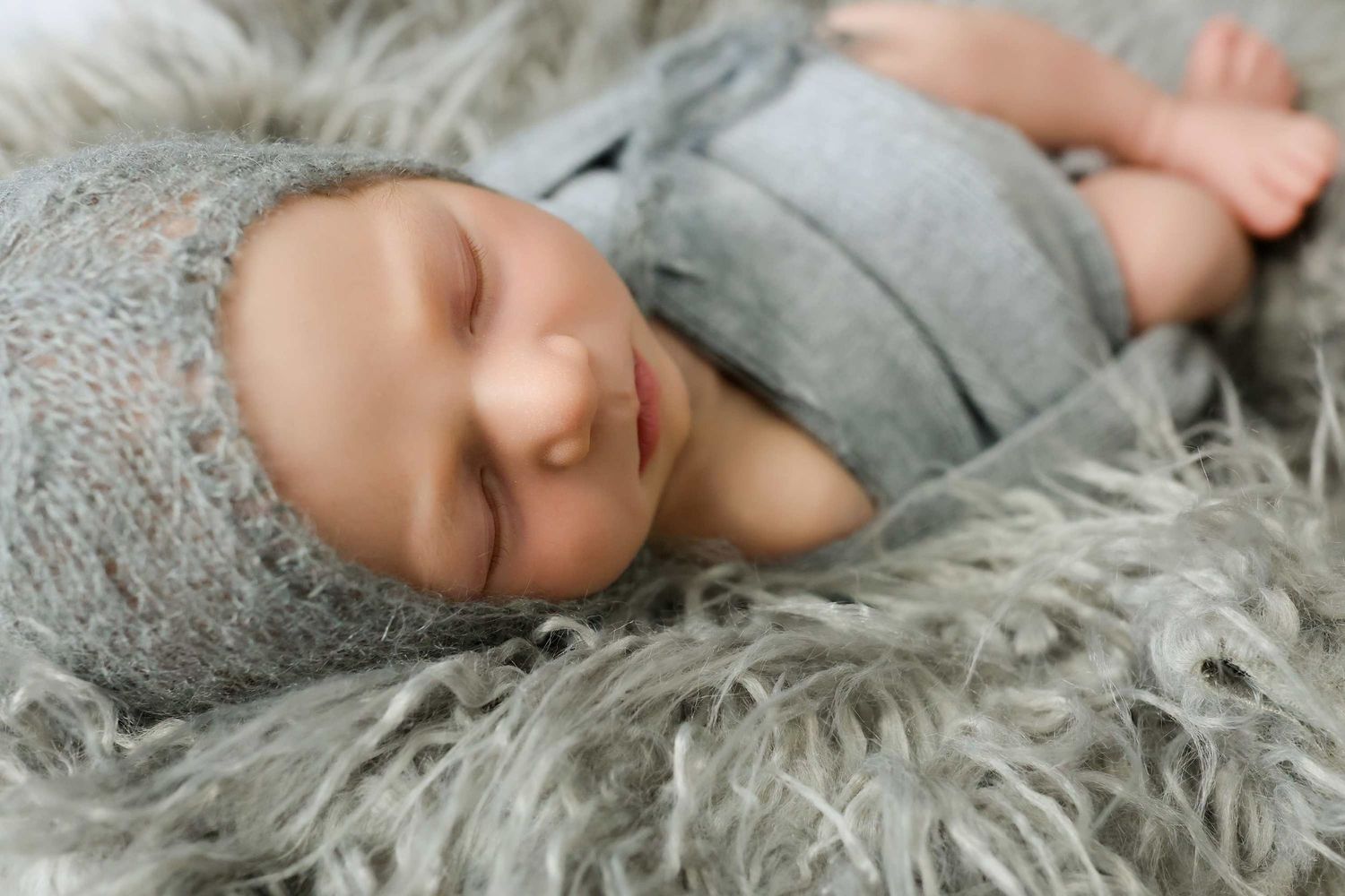 Newborn baby sleeping peacefully on cozy grey fur blanket during portrait session.