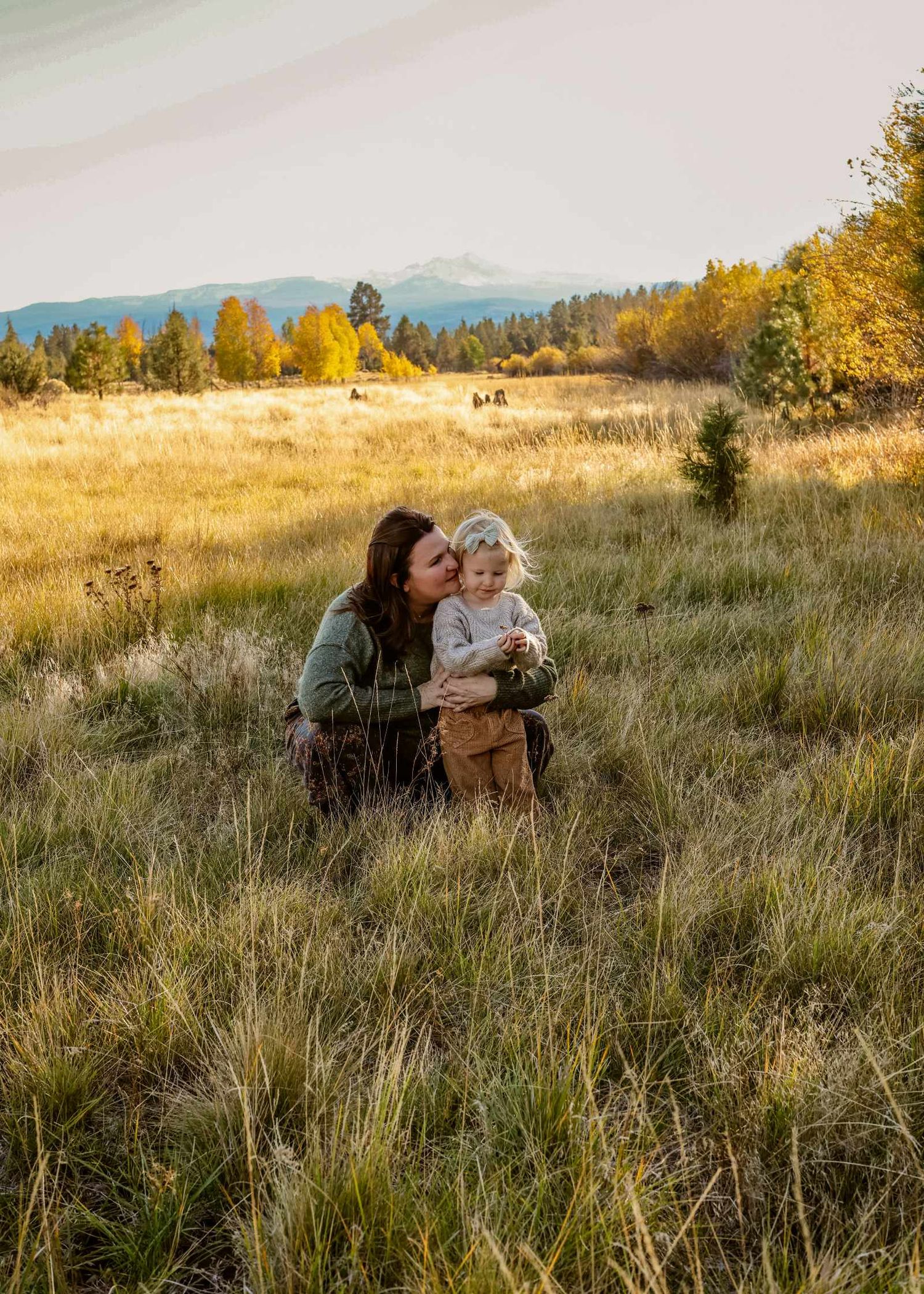 People sit together in a golden autumn field at sunset with mountains visible in the distance.