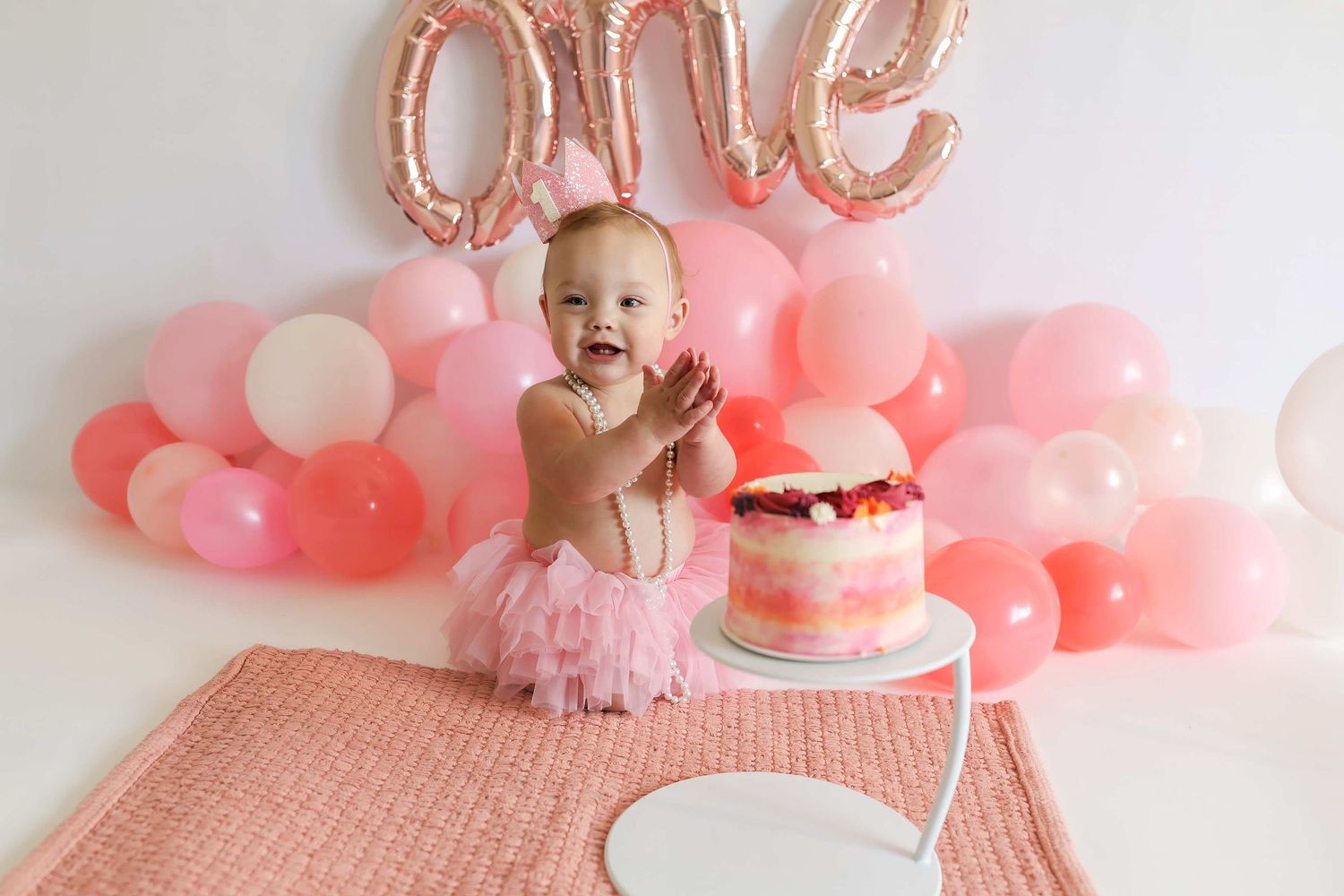 Pink and gold first birthday party setup with balloons, cake, and decorative details.