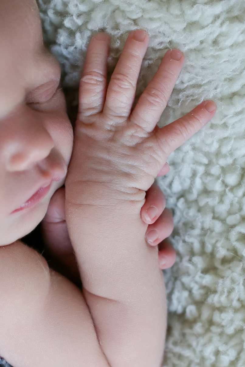 Close-up view of a baby's delicate hand resting against soft white textured fabric.