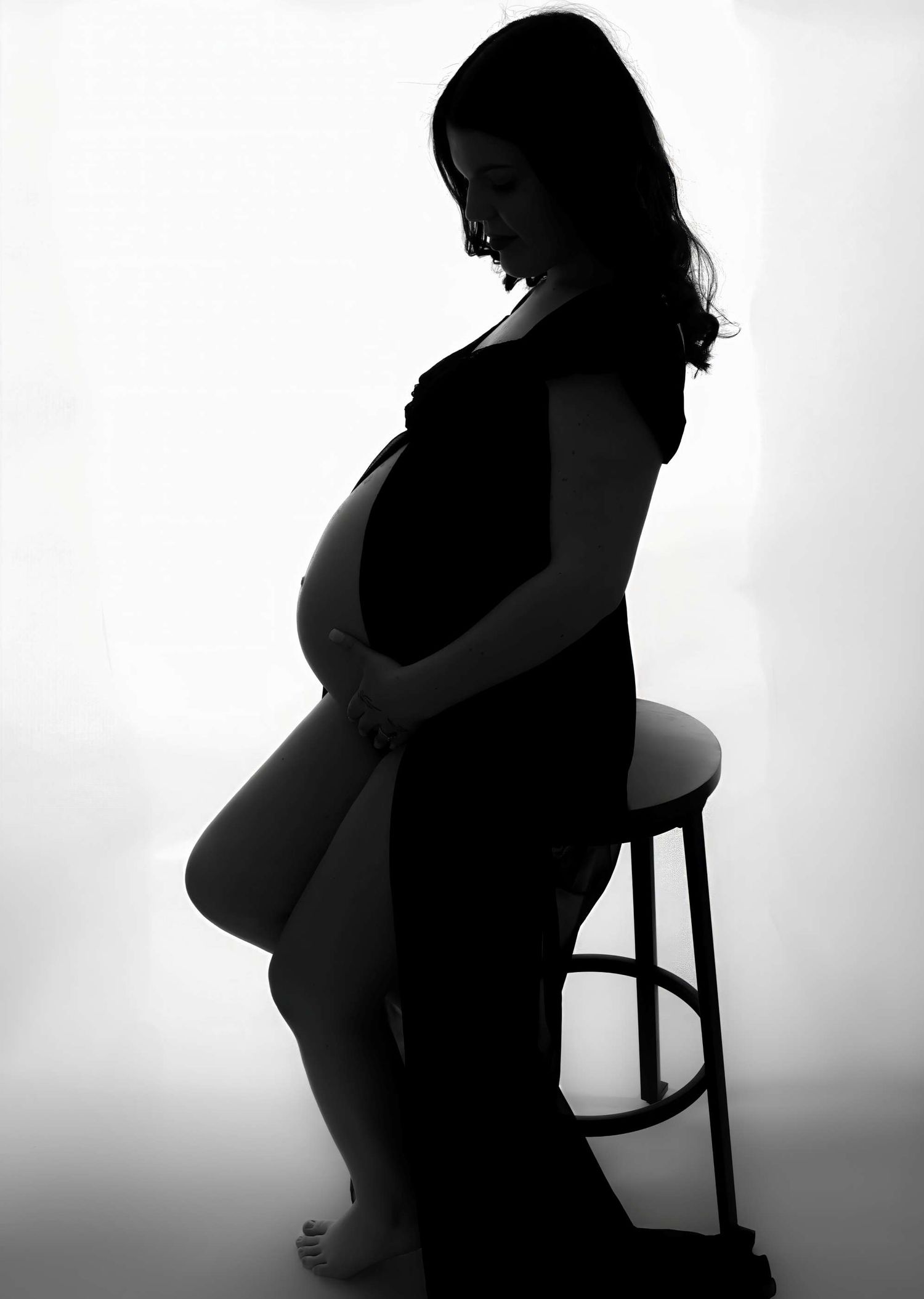 Dramatic silhouette of pregnant woman sitting on stool showing her baby bump profile.