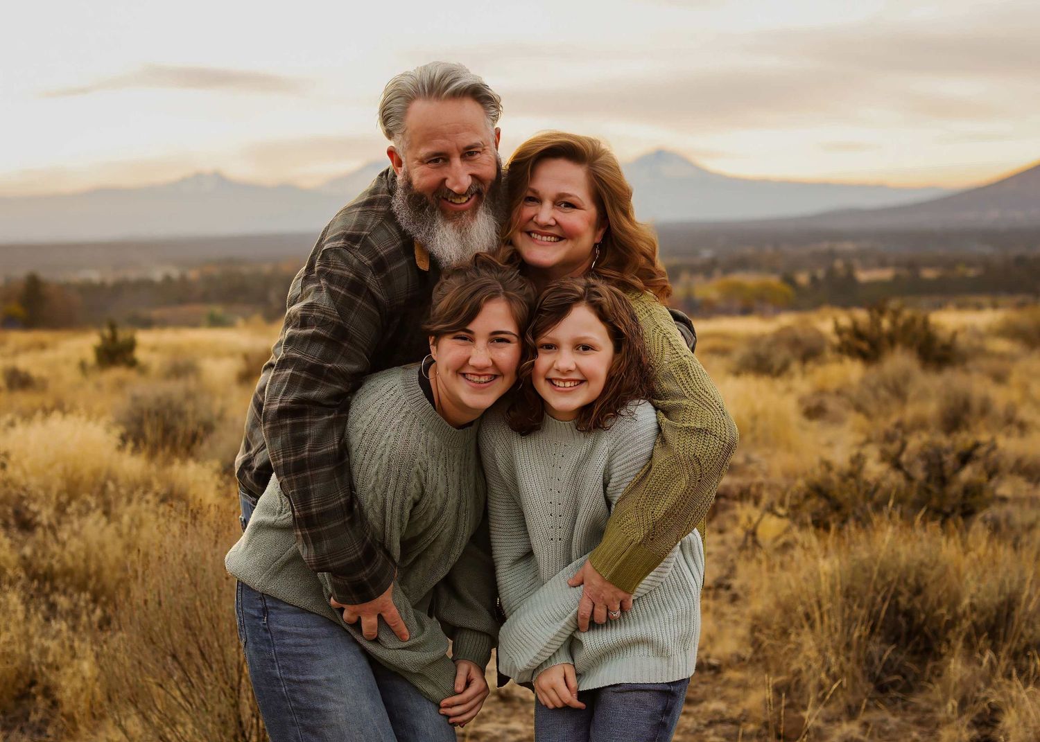 A couple embraces while standing in a desert landscape with mountains and sagebrush at sunset.