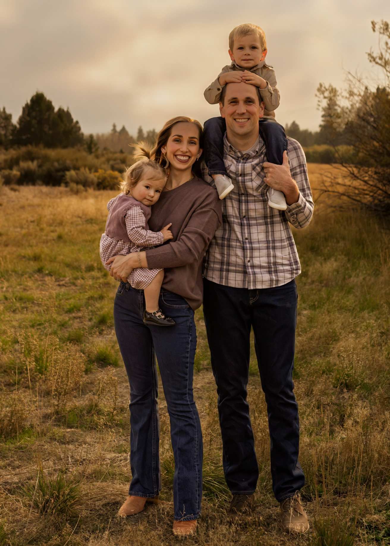 A family poses together in casual attire on a grassy hillside during golden hour.