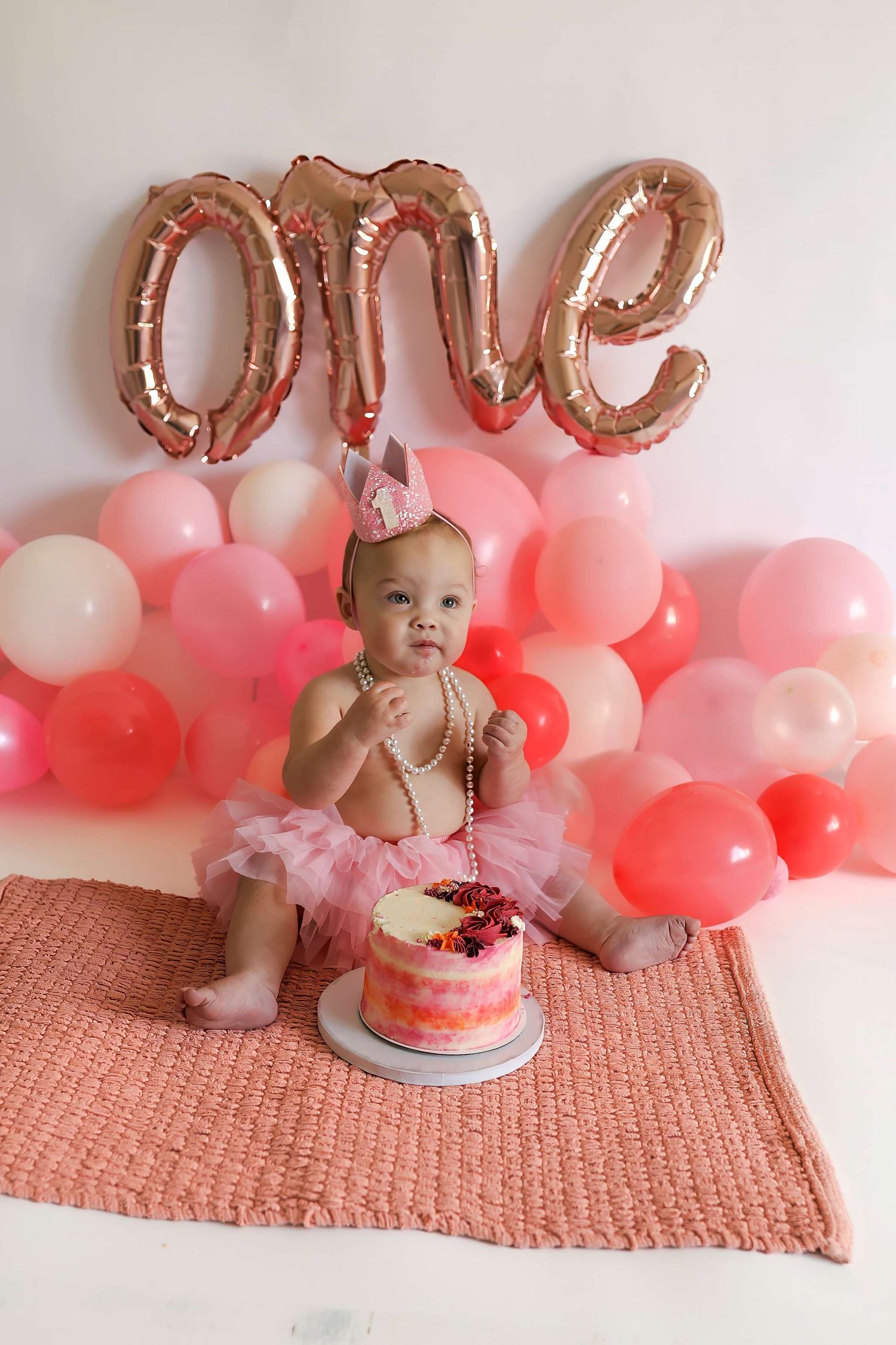 Baby's first birthday celebration setup with pink and white balloons, a cake, and rose gold letter decorations.