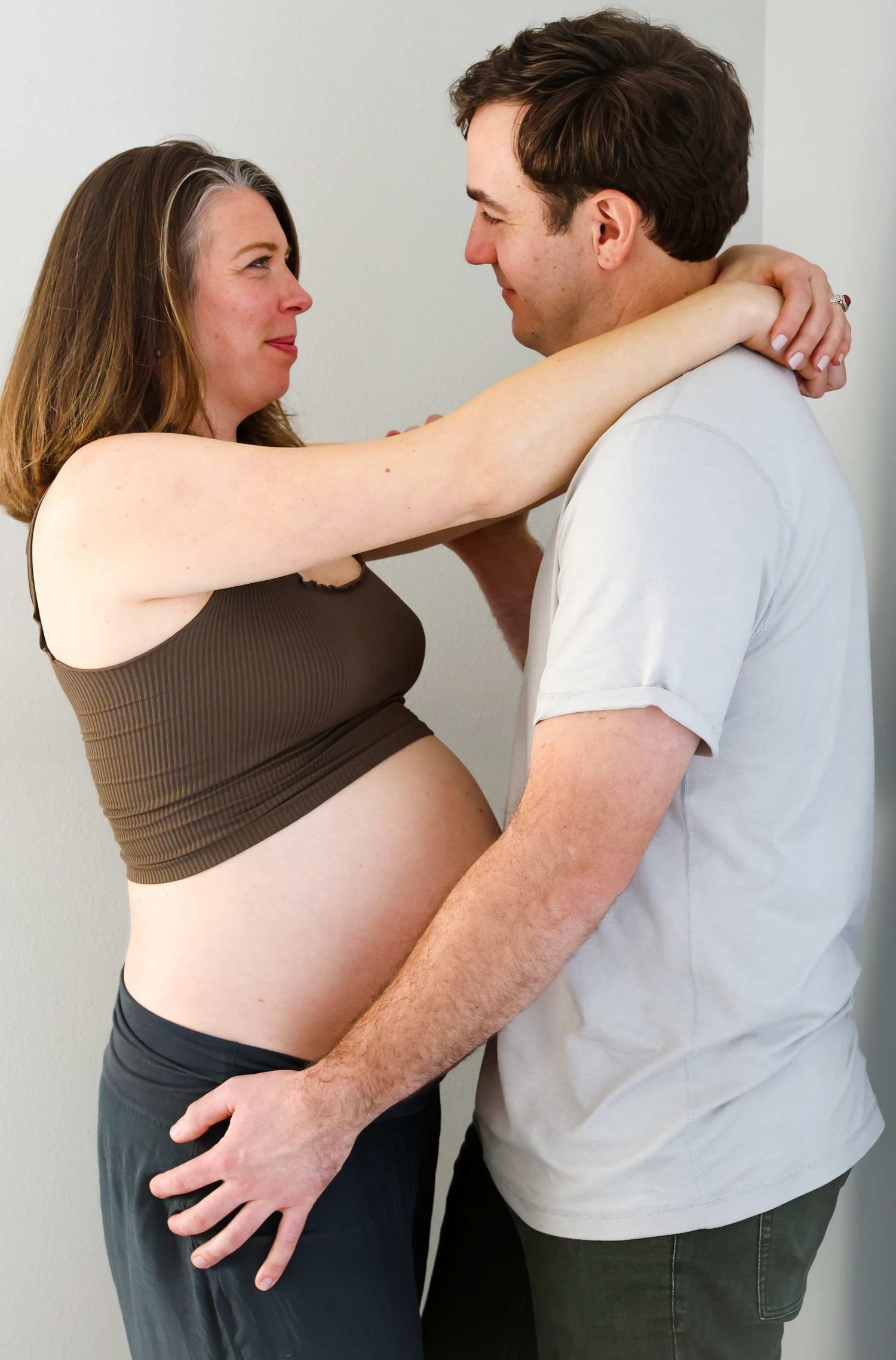 A couple shares an intimate moment as they embrace, with the woman wearing a brown crop top showing her pregnant belly.