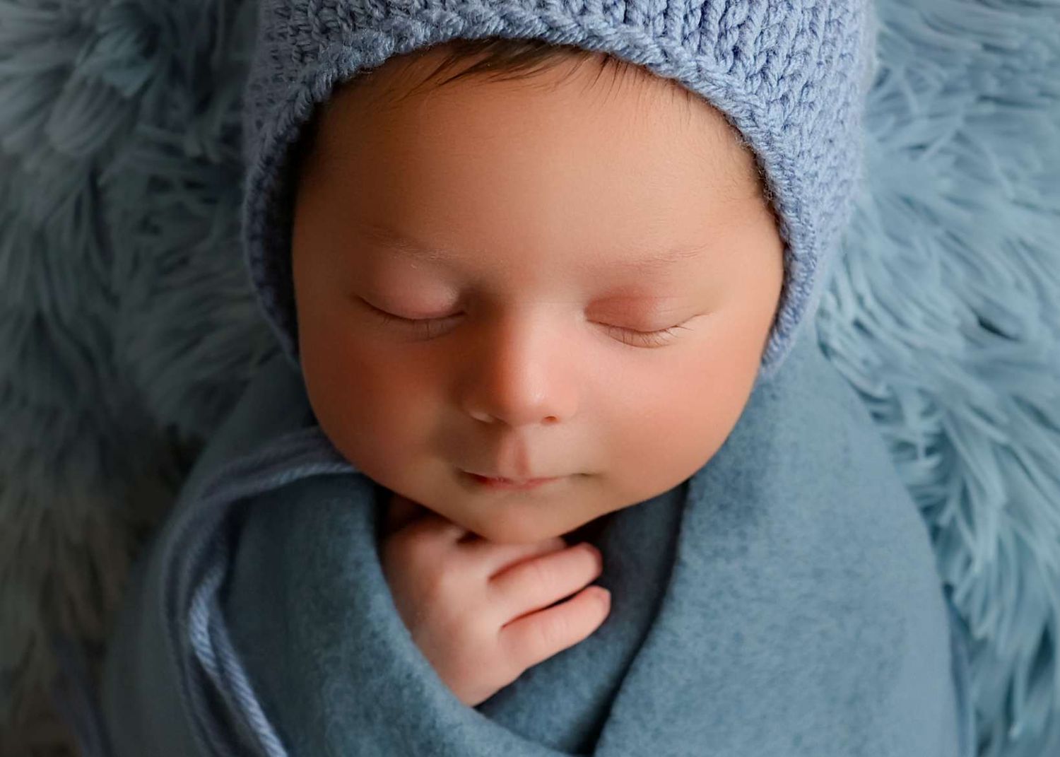Peaceful newborn baby sleeping wrapped in a soft blue blanket wearing a knit blue bonnet hat.