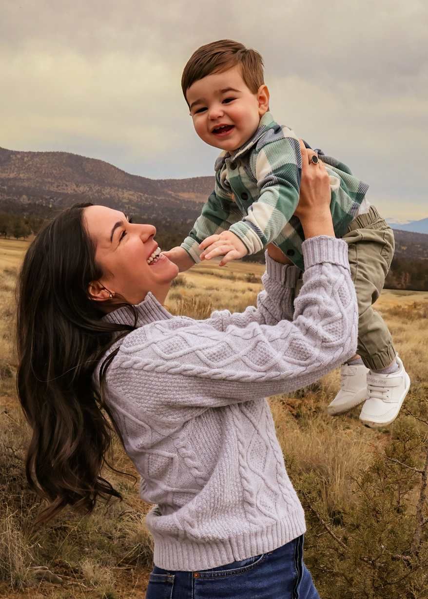 A parent and child share joyful moments together in a field with mountains visible in the background.