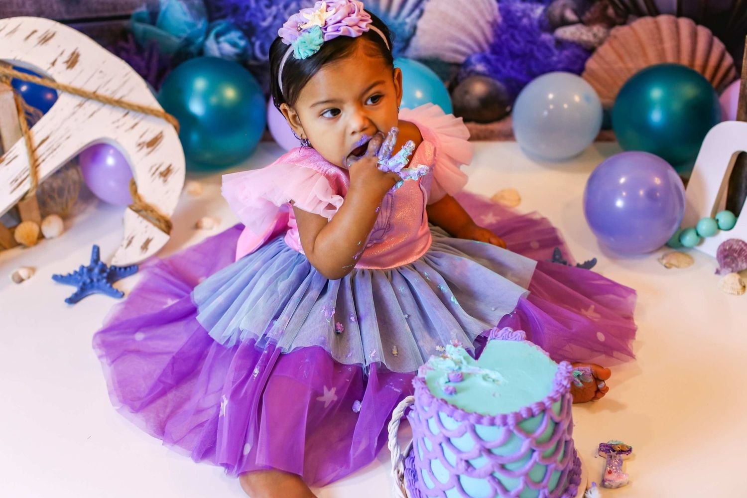 Baby girl in purple mermaid tutu dress celebrating first birthday with cake smash and ocean-themed decorations. Redmond Oregon Studio