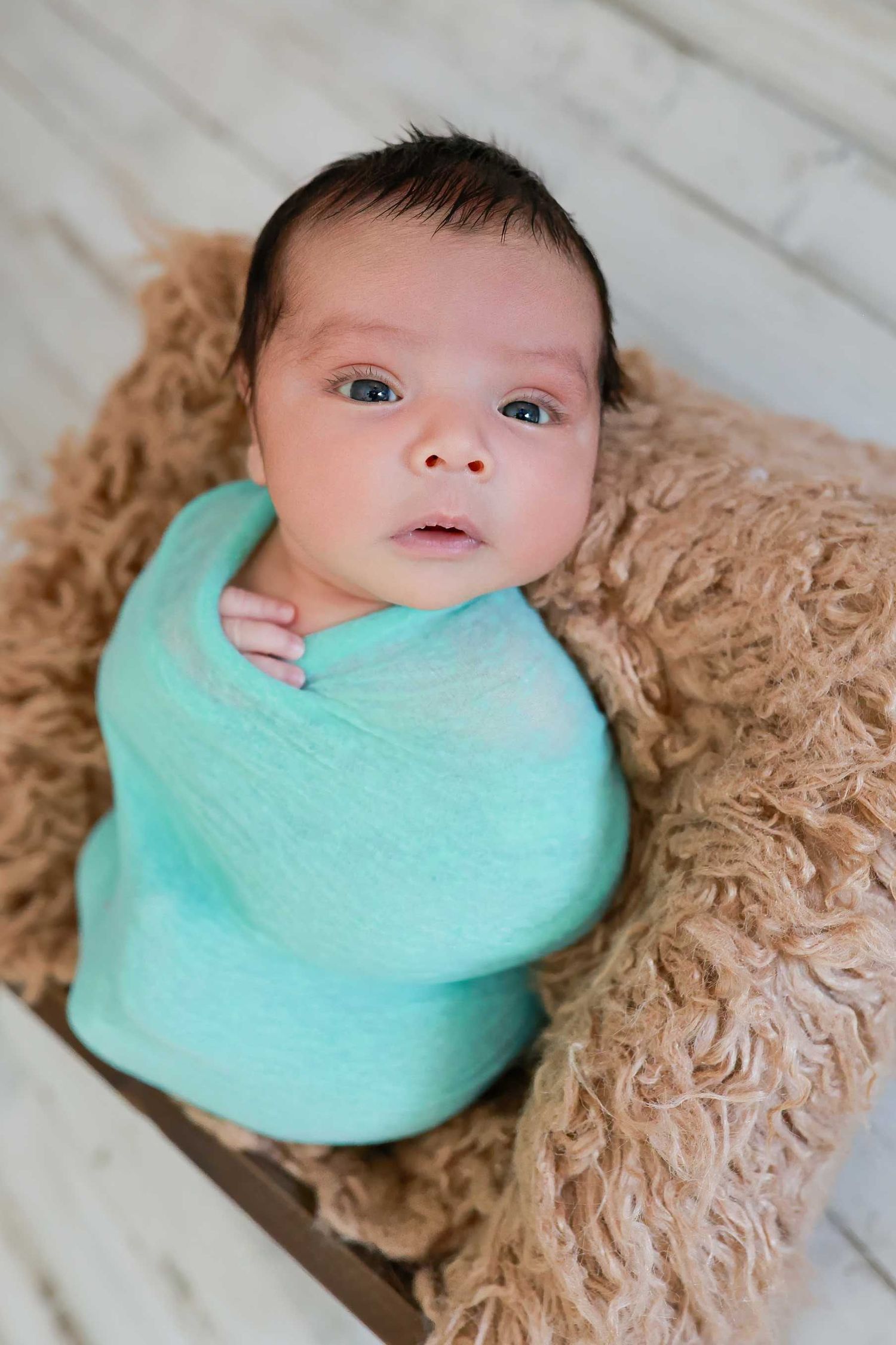 Newborn portrait series with baby wrapped in mint green swaddle on beige textured backdrop.