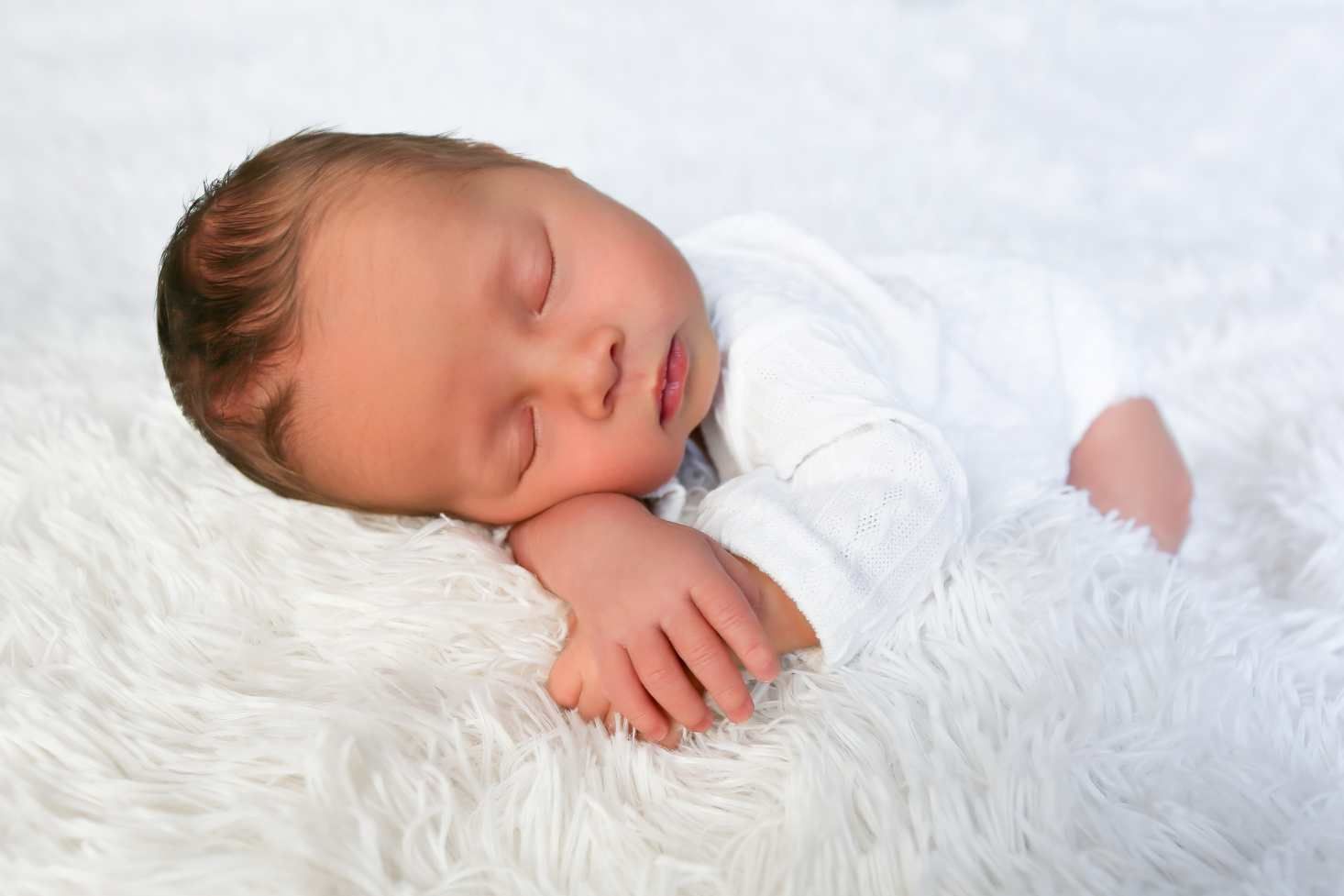 Peaceful baby resting on soft white textured blanket in gentle natural light.