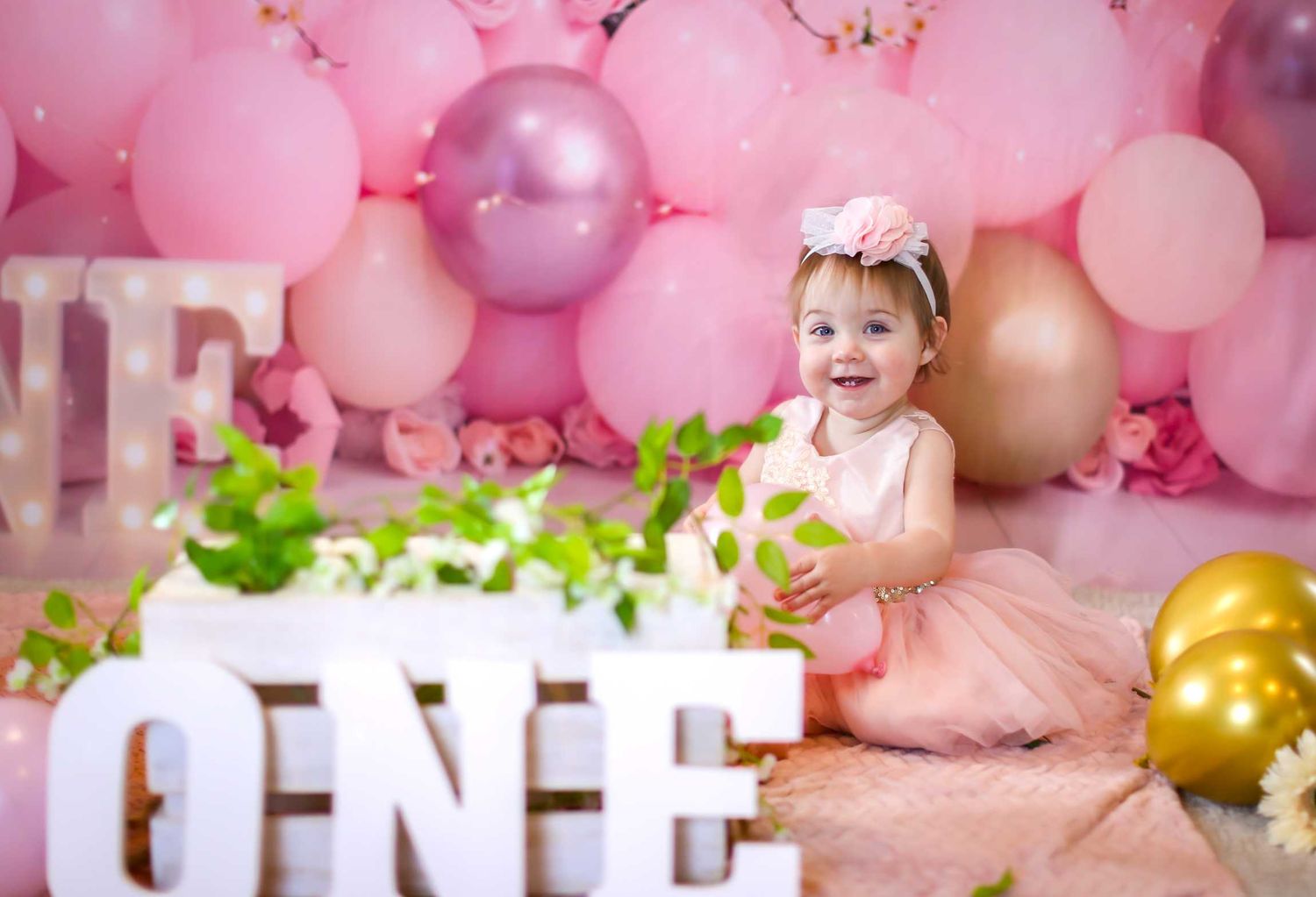 Pink and gold balloon arch decorates a first birthday celebration with ONE letters and tulle dress.