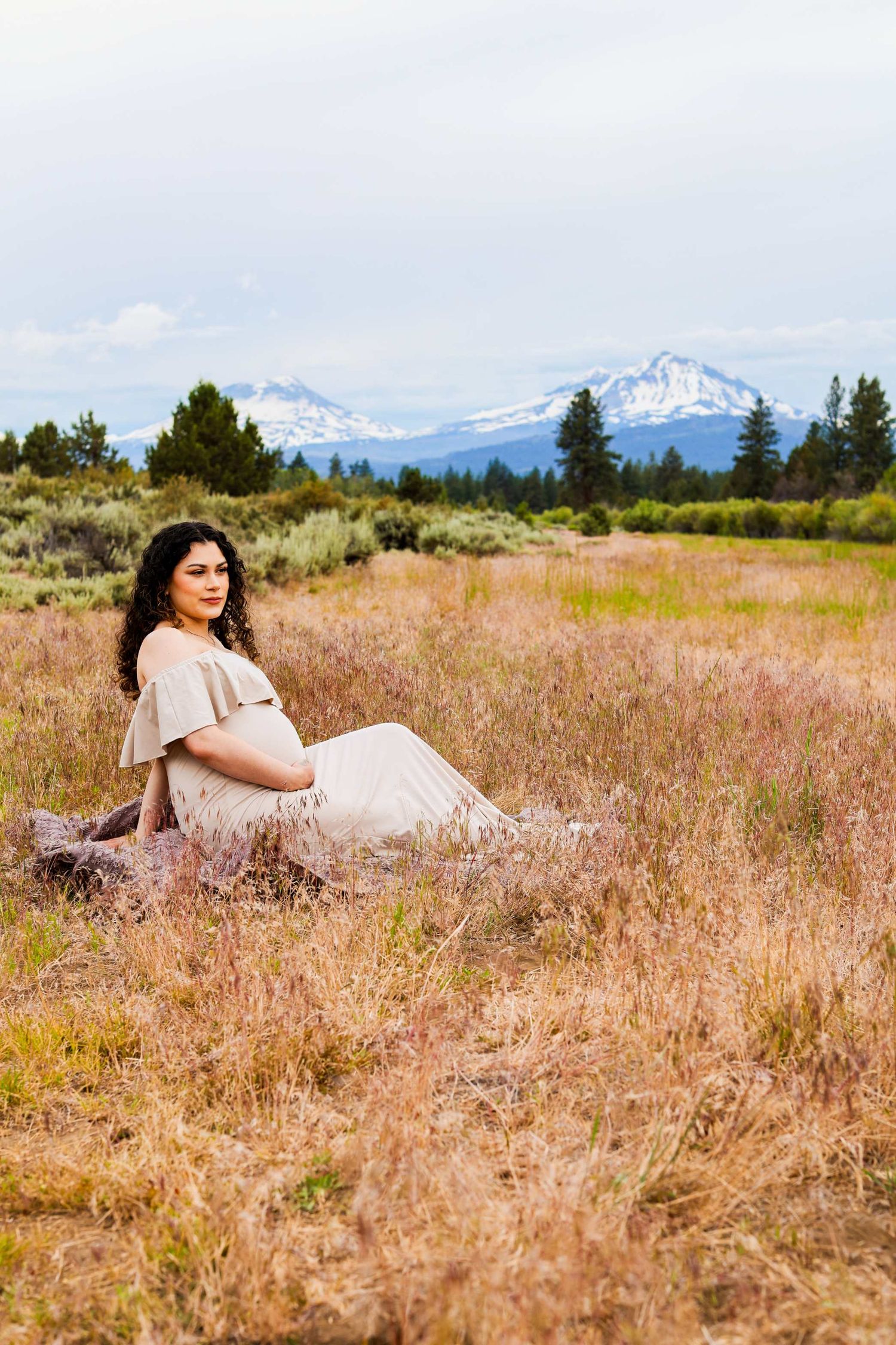 Maternity photoshoot in a golden field with snow-capped mountains in the background.