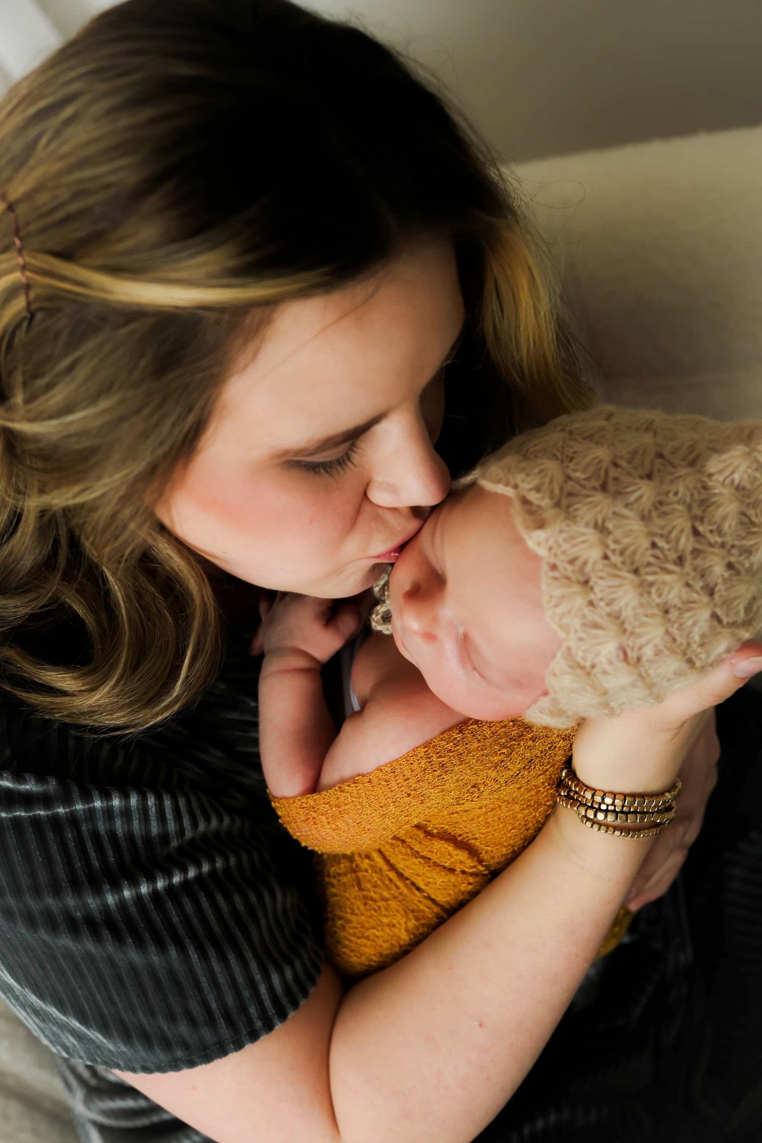 Tender moment between parent and baby wrapped in mustard yellow blanket with soft natural lighting.