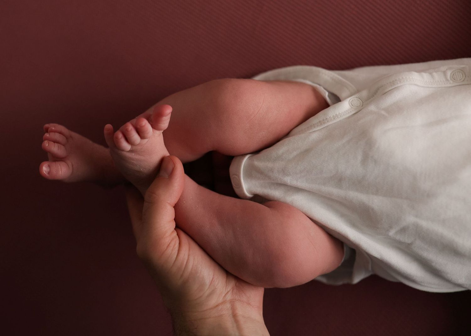 A close-up photo sequence showing a hand gently cradling a newborn baby's tiny foot against a dark background.