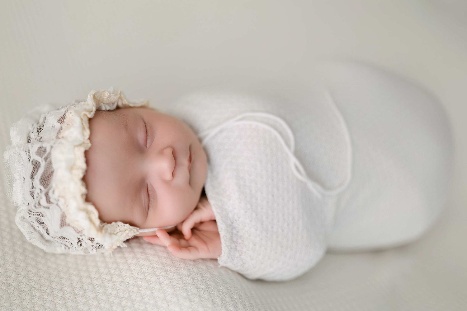 Sleeping newborn baby wrapped in white swaddle on soft textured blanket.