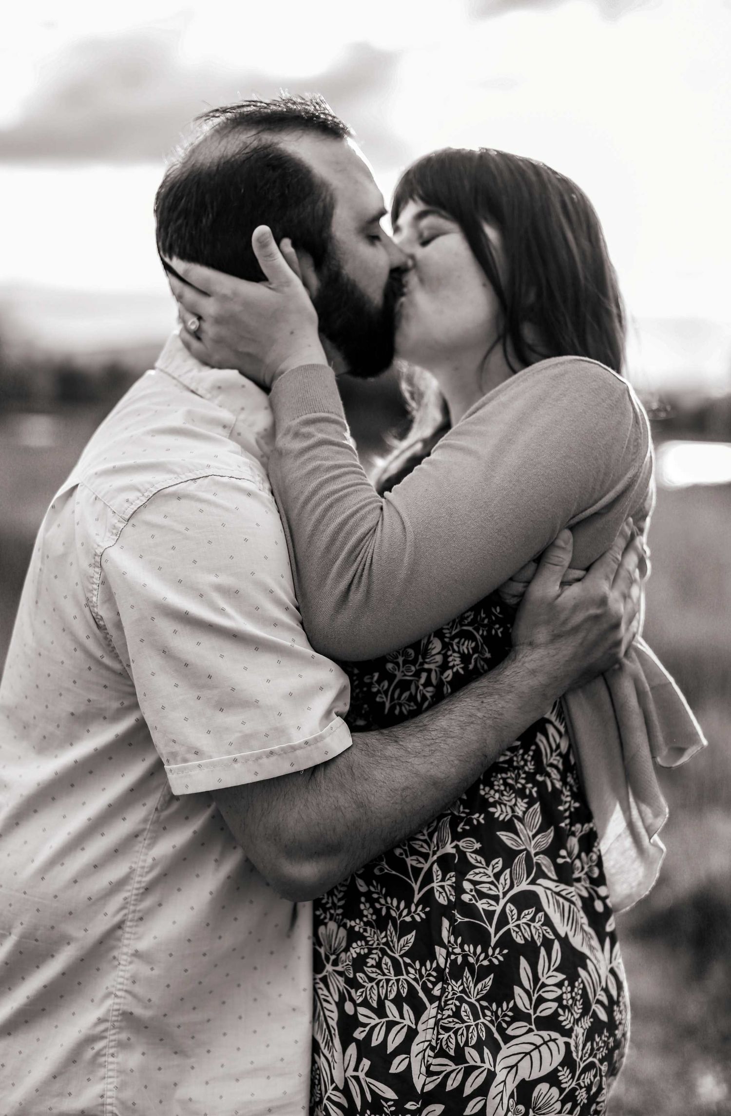 Couple sharing a romantic kiss outdoors in a black and white portrait photograph.