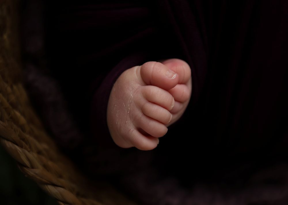 Close-up of a newborn baby's tiny clenched fist resting against dark fabric.