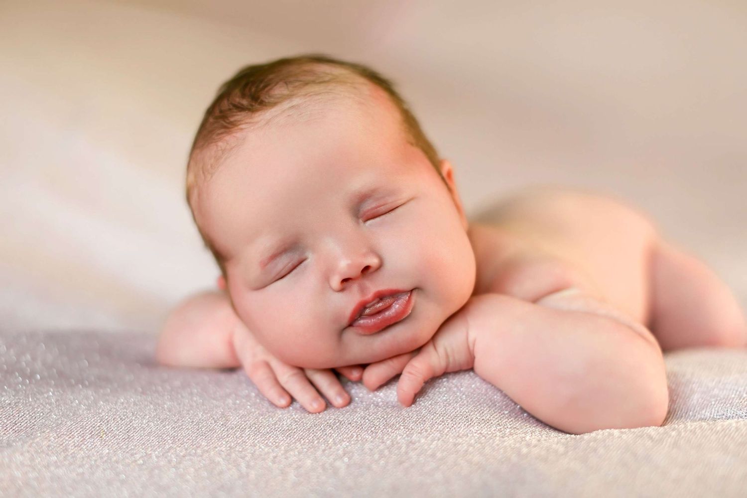 Sweet sleeping newborn rests peacefully on soft gray blanket with tiny smile.