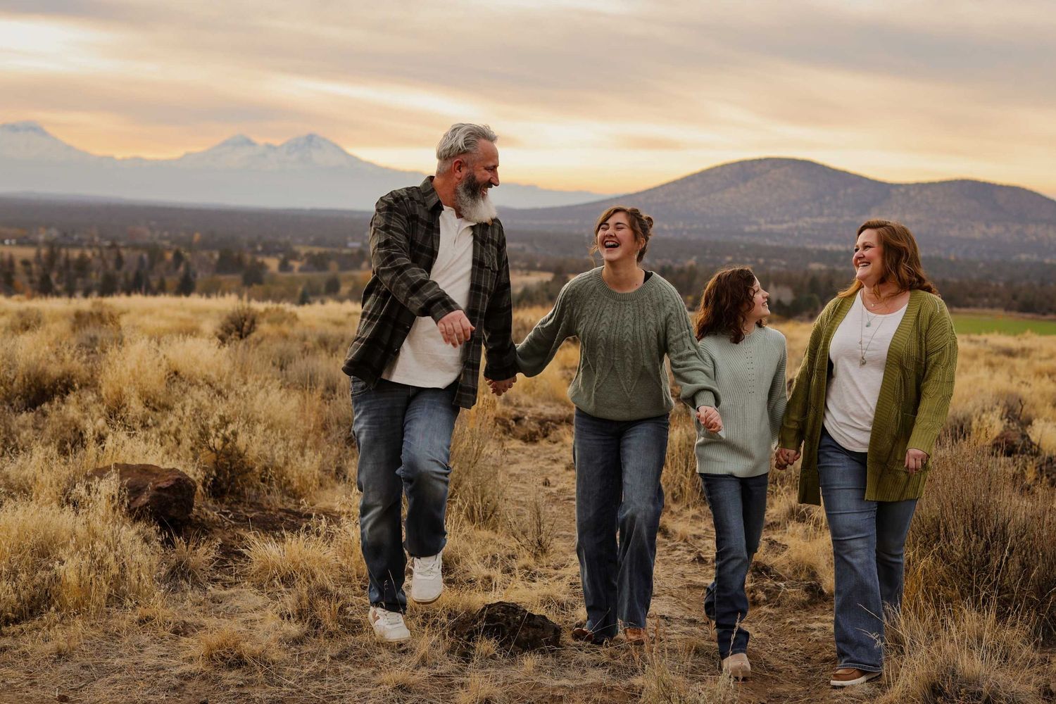 People walking through golden grass in a field at sunset with mountains in the background. Redmond Oregon