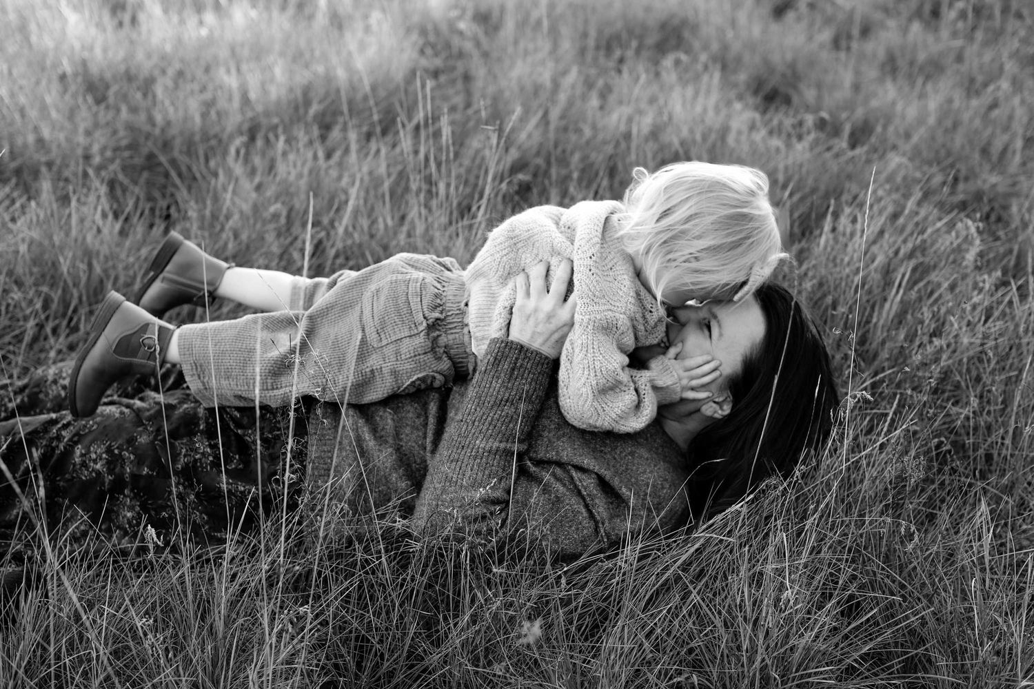 Black and white photo of a woman and young child sharing a tender moment lying in a grassy field.