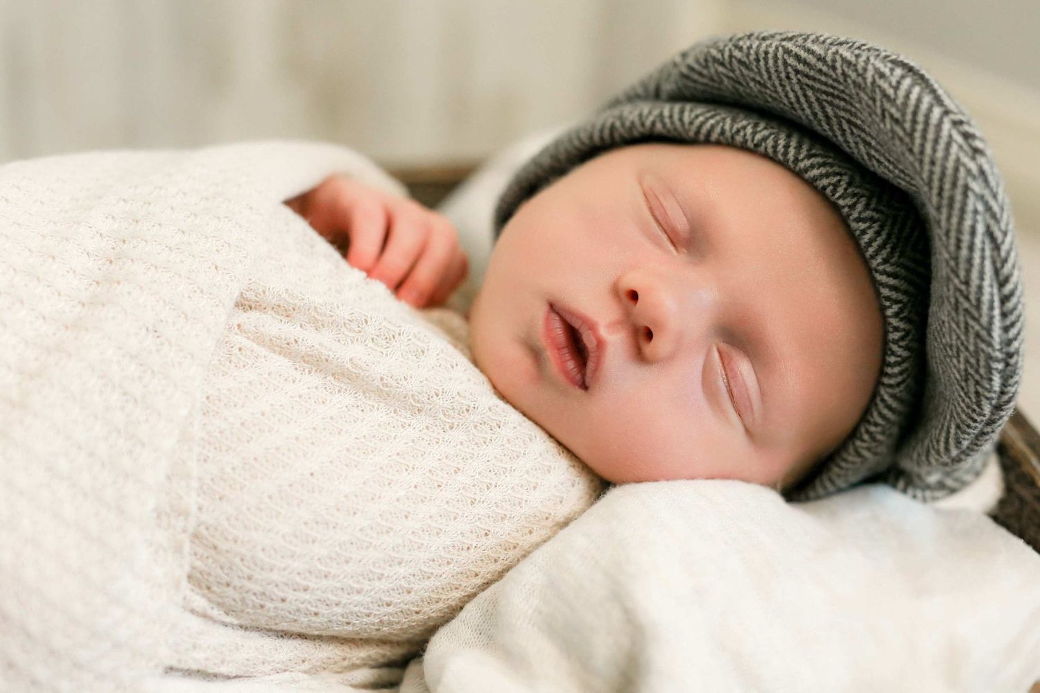 Sleeping baby wrapped in white blanket wearing gray knit beanie hat.