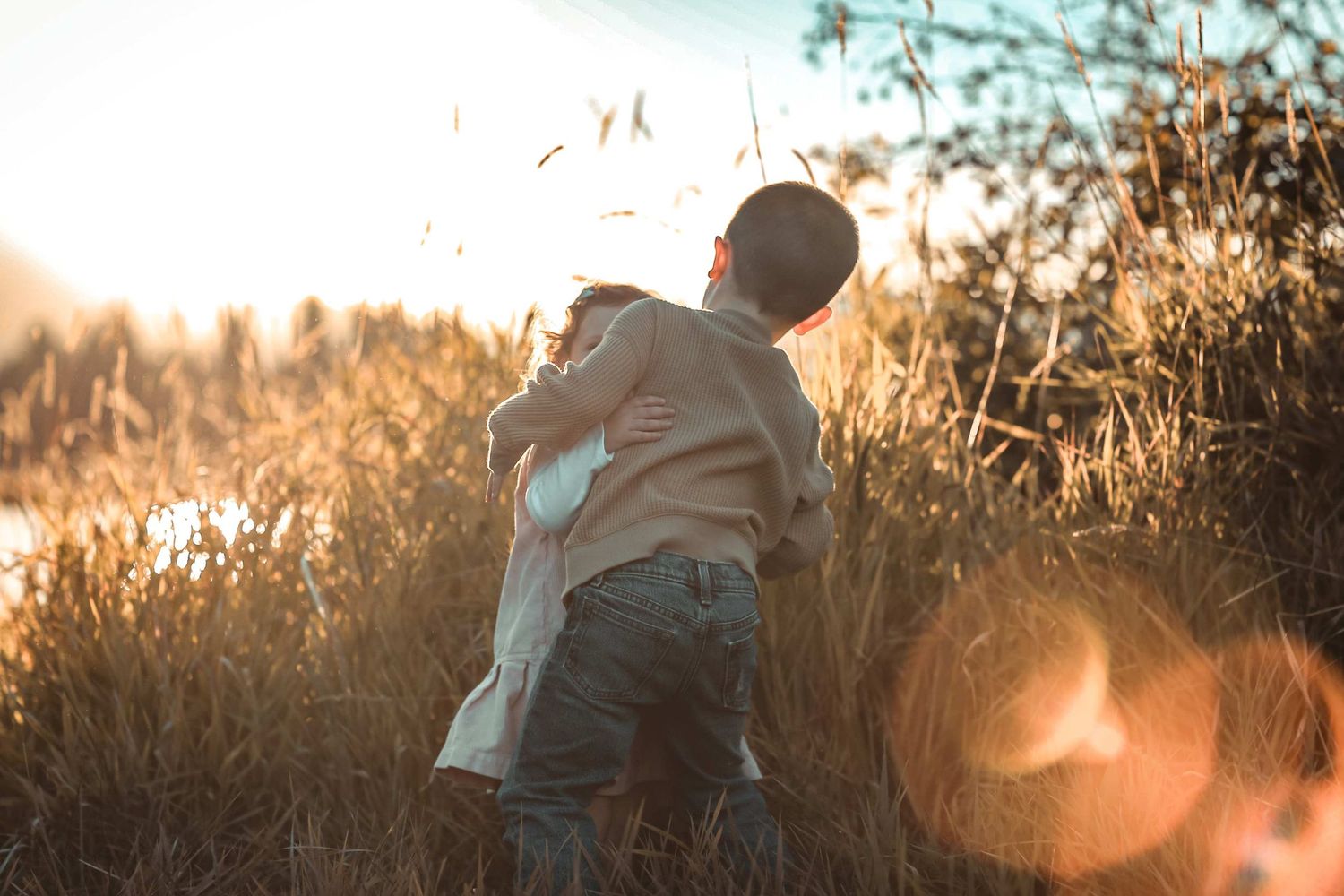 Family members share tender moments along a wooden fence at sunset with warm golden light filtering through.