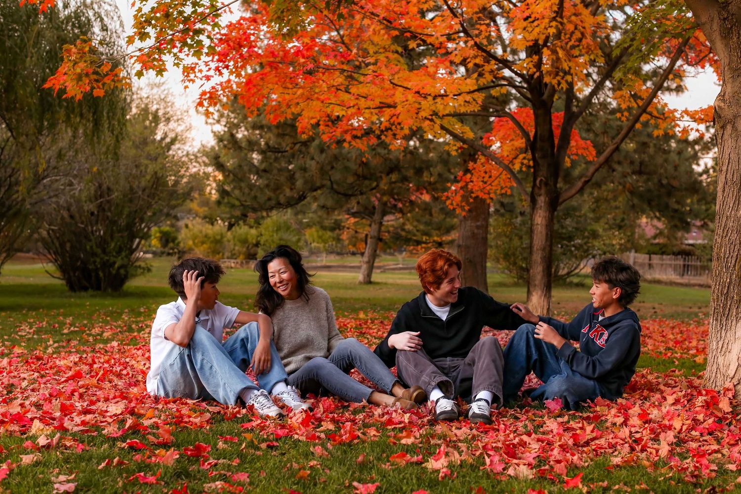 Group relaxing on blanket under vibrant orange fall foliage in park setting.