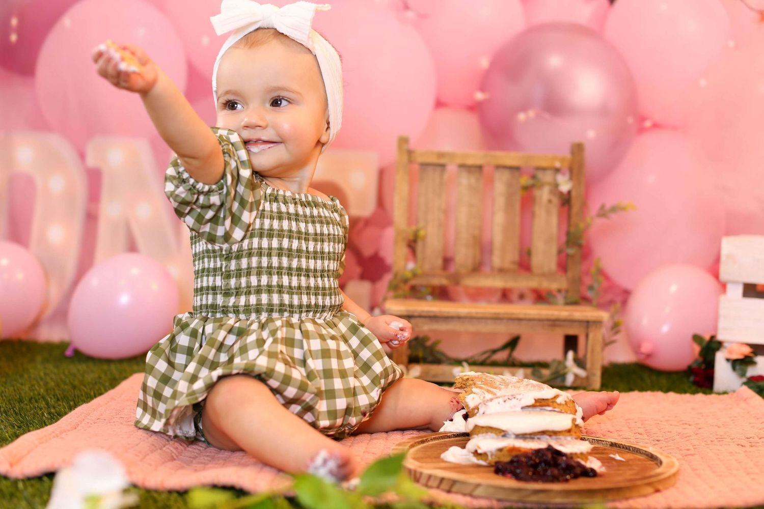 Pink themed first birthday party setting with wooden furniture and balloon decorations.