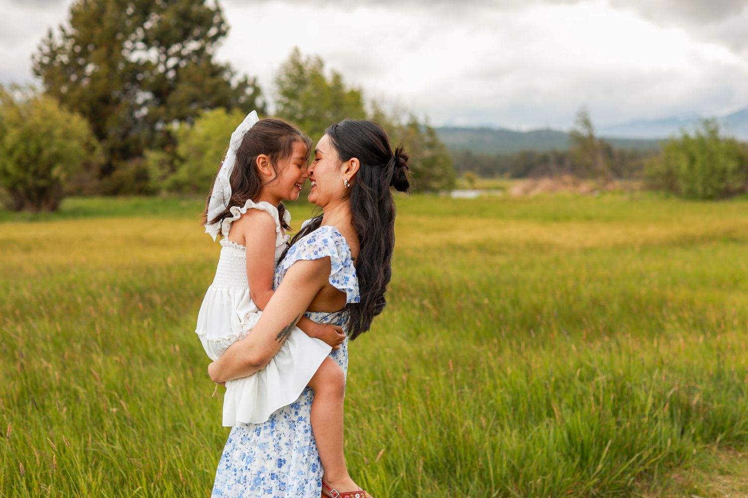 A mother holds her young daughter in a lush green meadow, the two sharing a nose-to-nose moment outdoors. Black Butte Ranch Sisters  Oregon