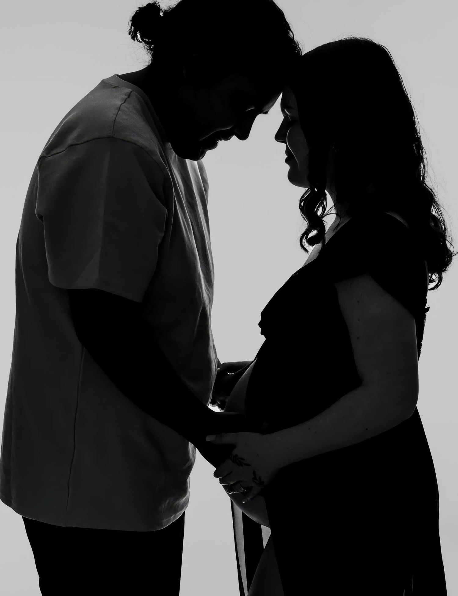 Dramatic silhouette of couple sharing intimate moment during pregnancy photoshoot.