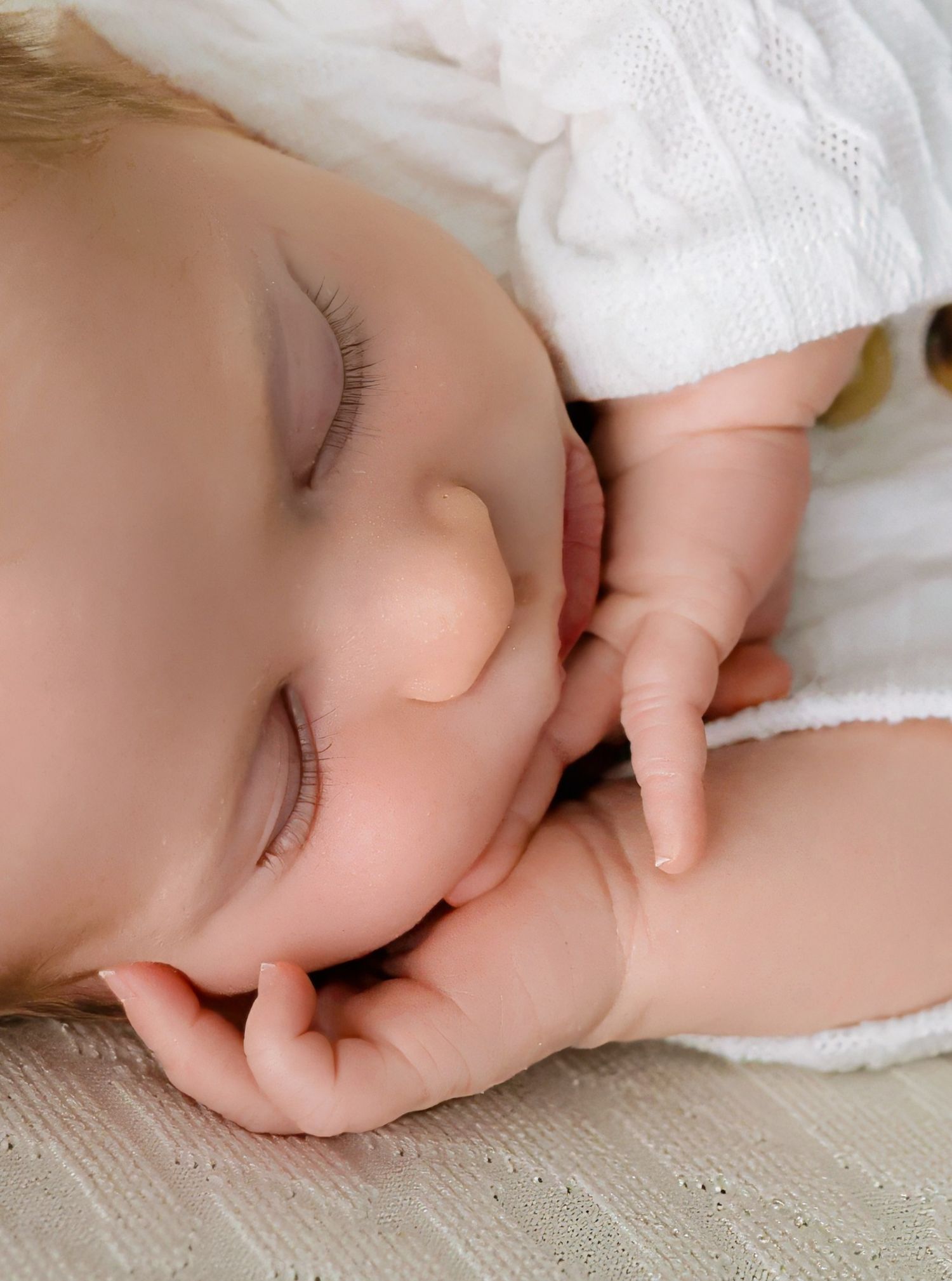 Close-up series of sleeping baby's hands against white textured fabric background.