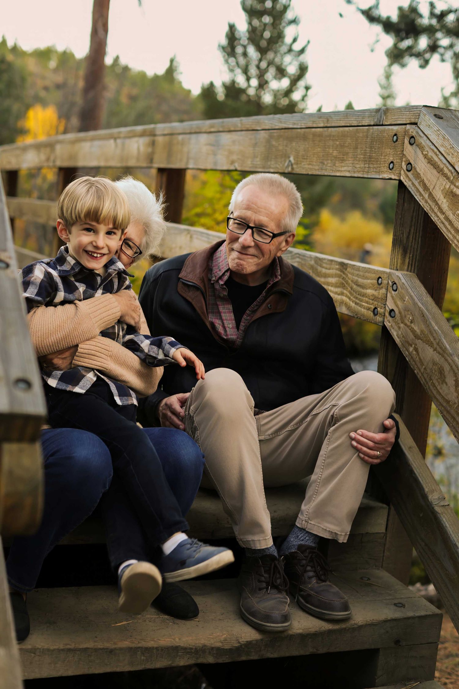 Two photographers sit on wooden stairs reviewing photos on their cameras in an outdoor setting during autumn.