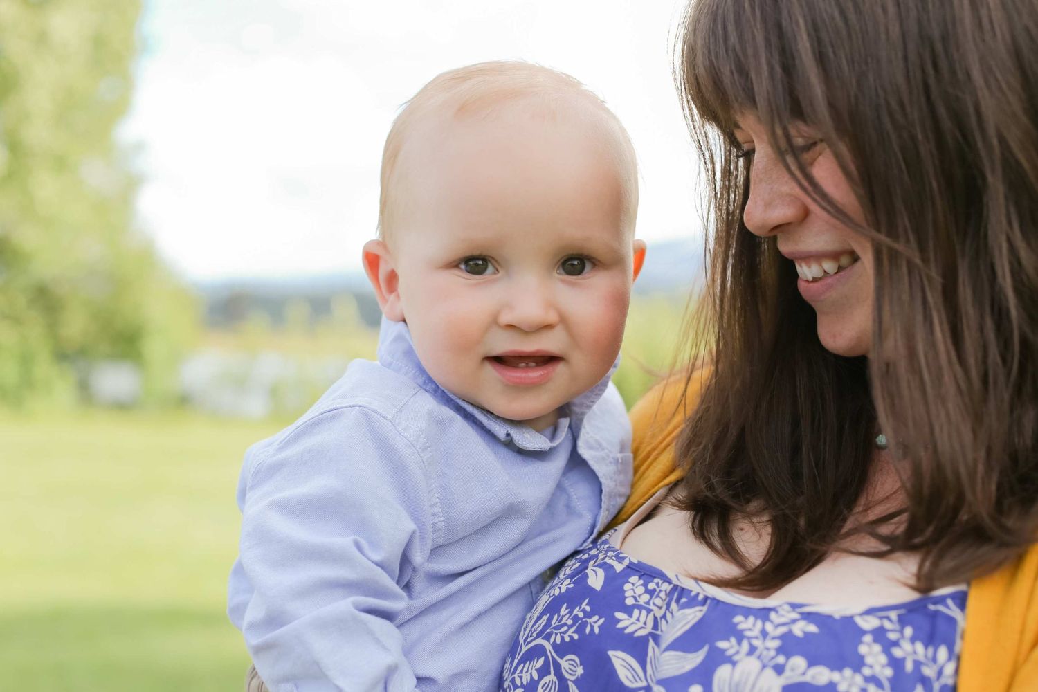 A tender outdoor family moment captured in bright natural sunlight with a baby in light blue clothing.