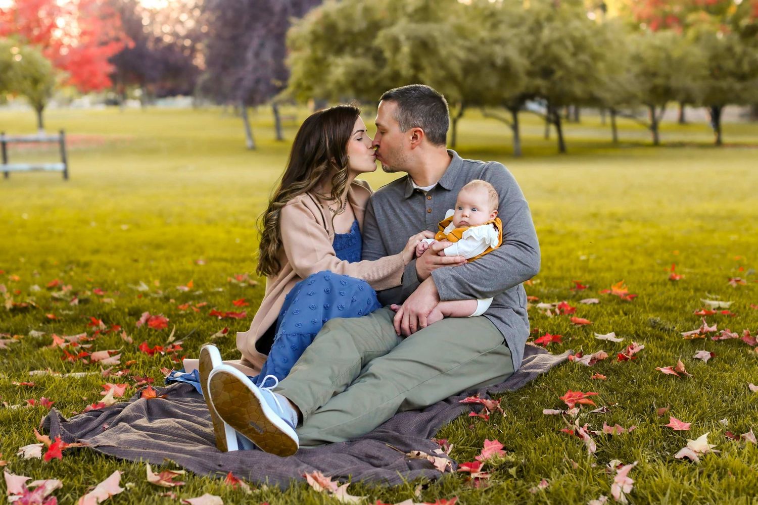 Couple relaxing together on a blanket in autumn park with colorful fall leaves scattered on the ground.