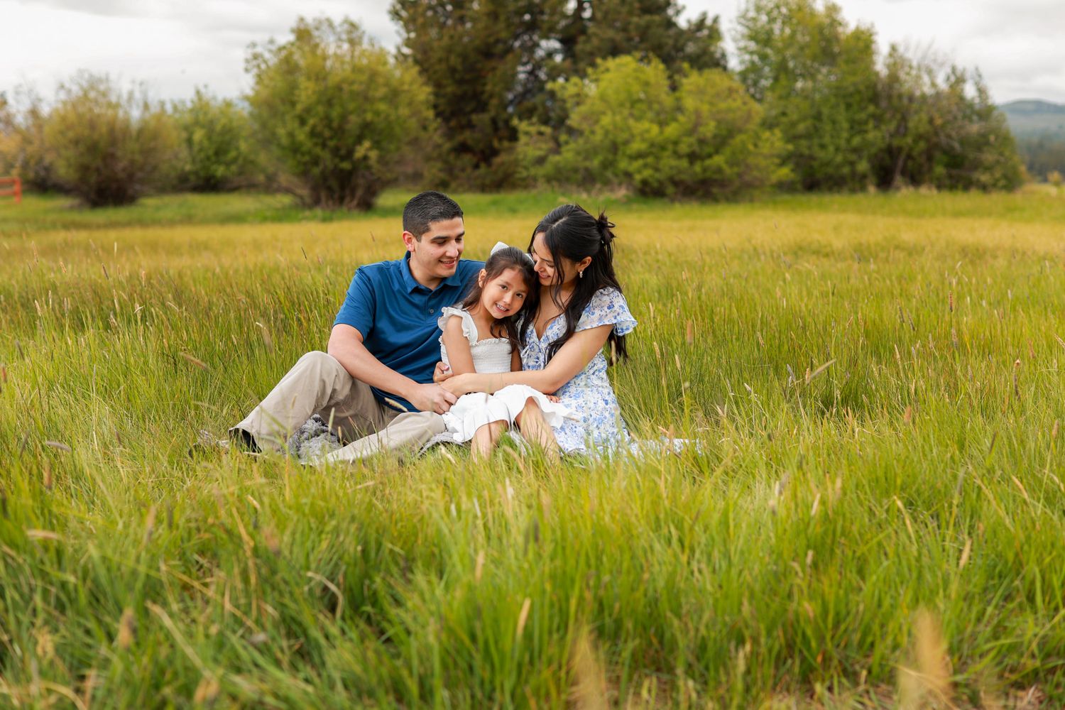 Family of three sitting together in a lush green meadow, sharing a joyful moment outdoors. Black Butte Ranch Sisters Oregon