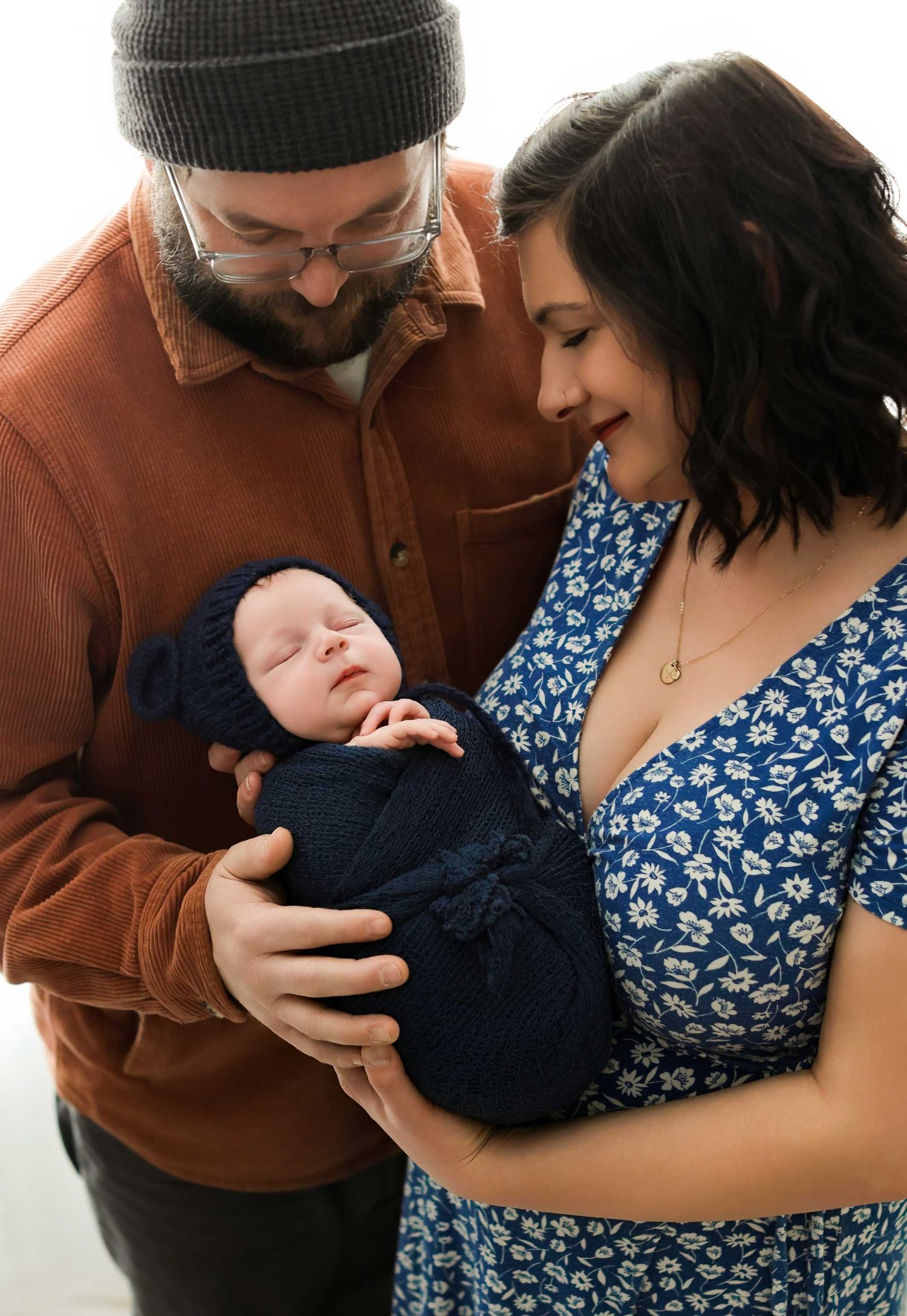 A series of intimate family moments showing parents cradling a newborn baby in a blue outfit.