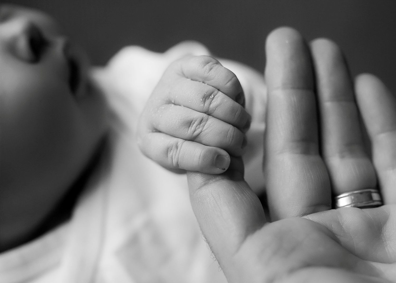 Intimate monochrome capture of interlaced newborn and parent fingers.