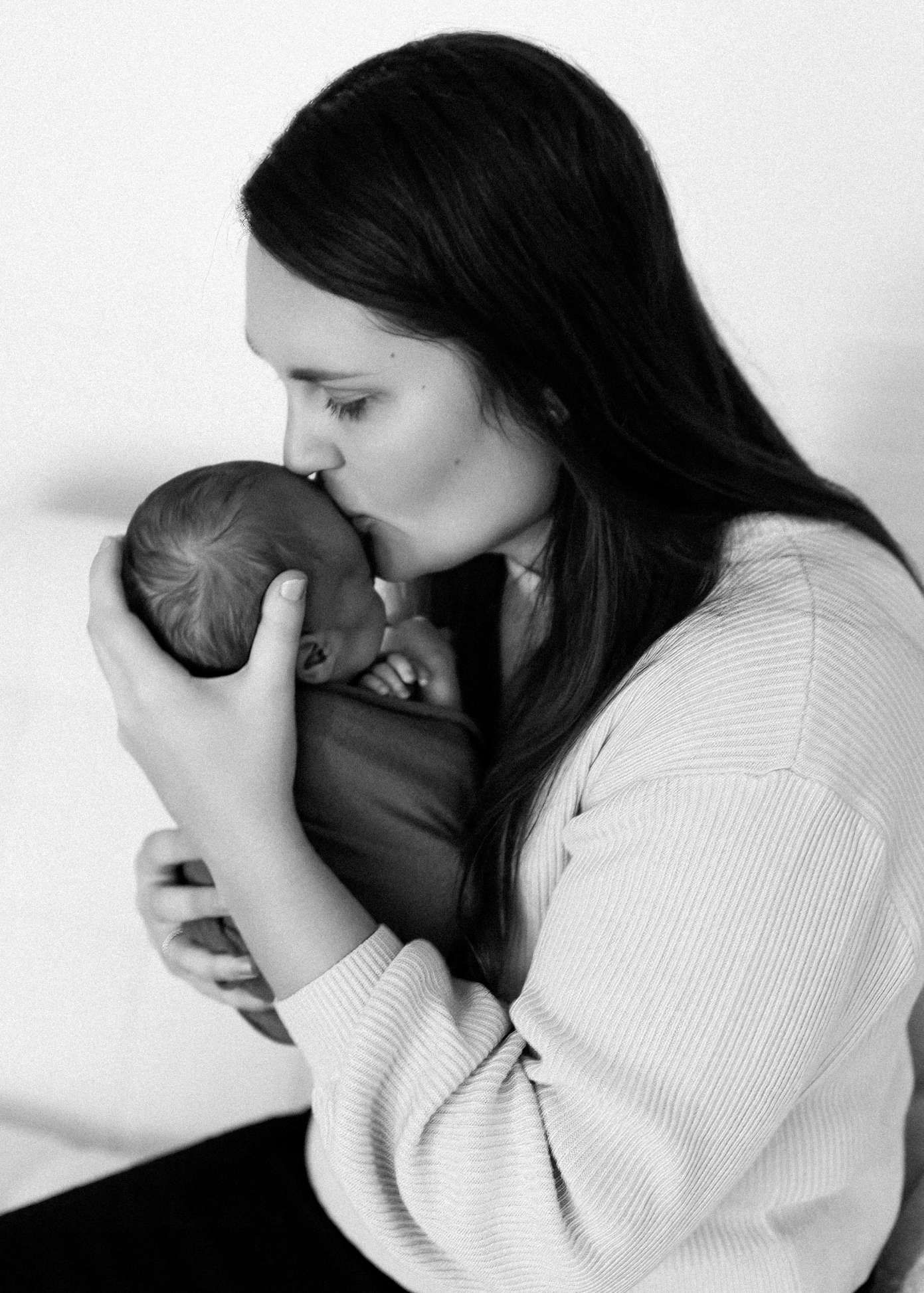 A series of four black and white photos showing tender moments between a parent and baby in matching white outfits.