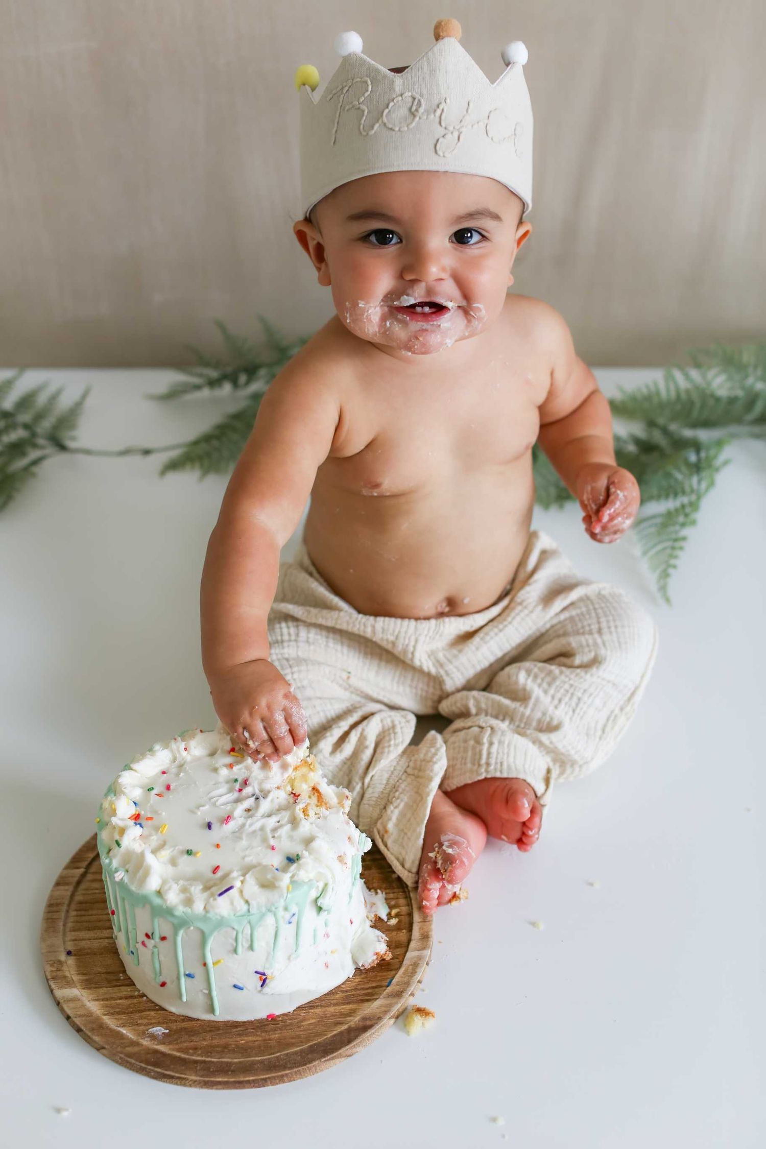 White cake smash photography session with rustic wooden plate and evergreen branch decorations.