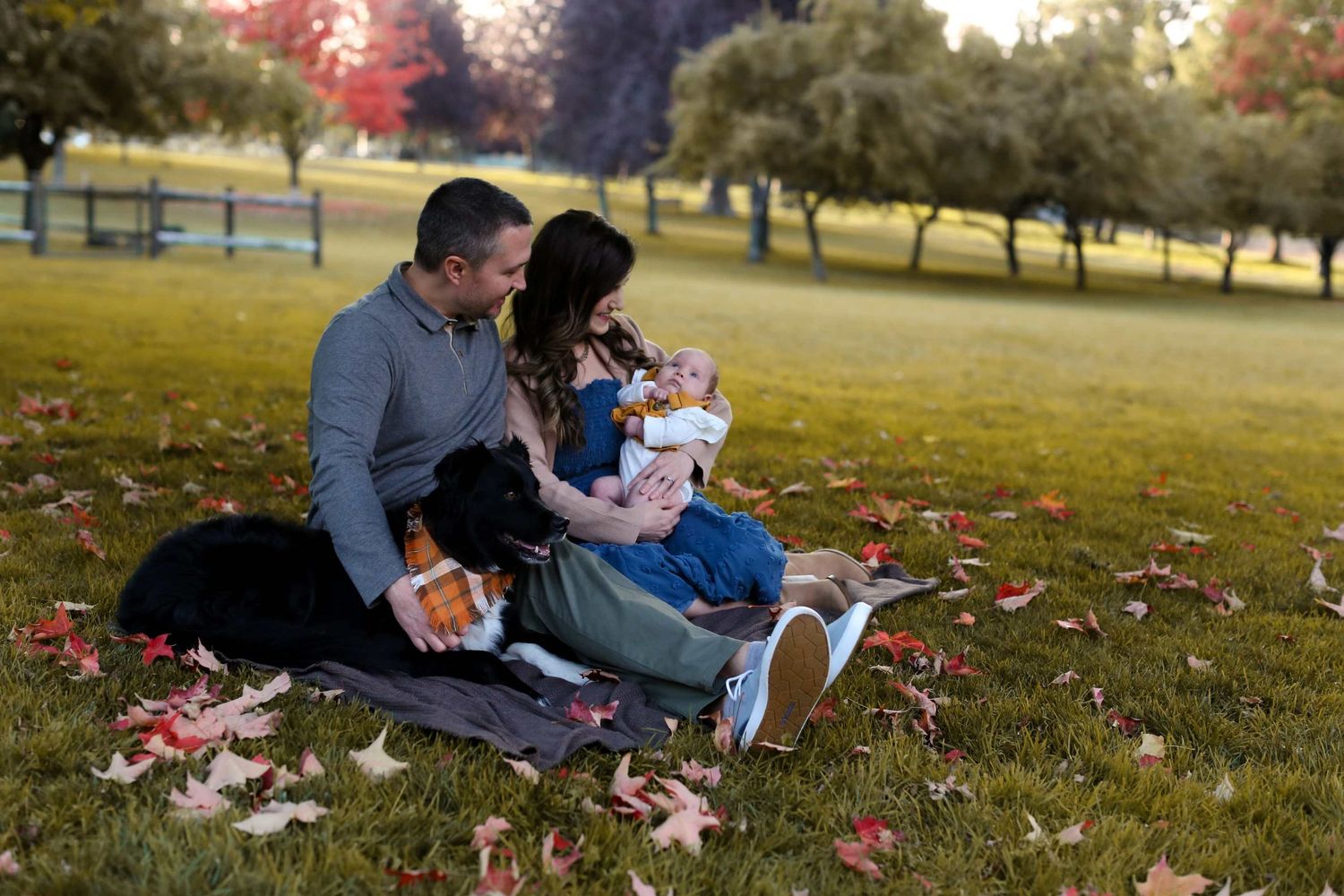Family enjoying a fall day together on grass covered with autumn leaves.