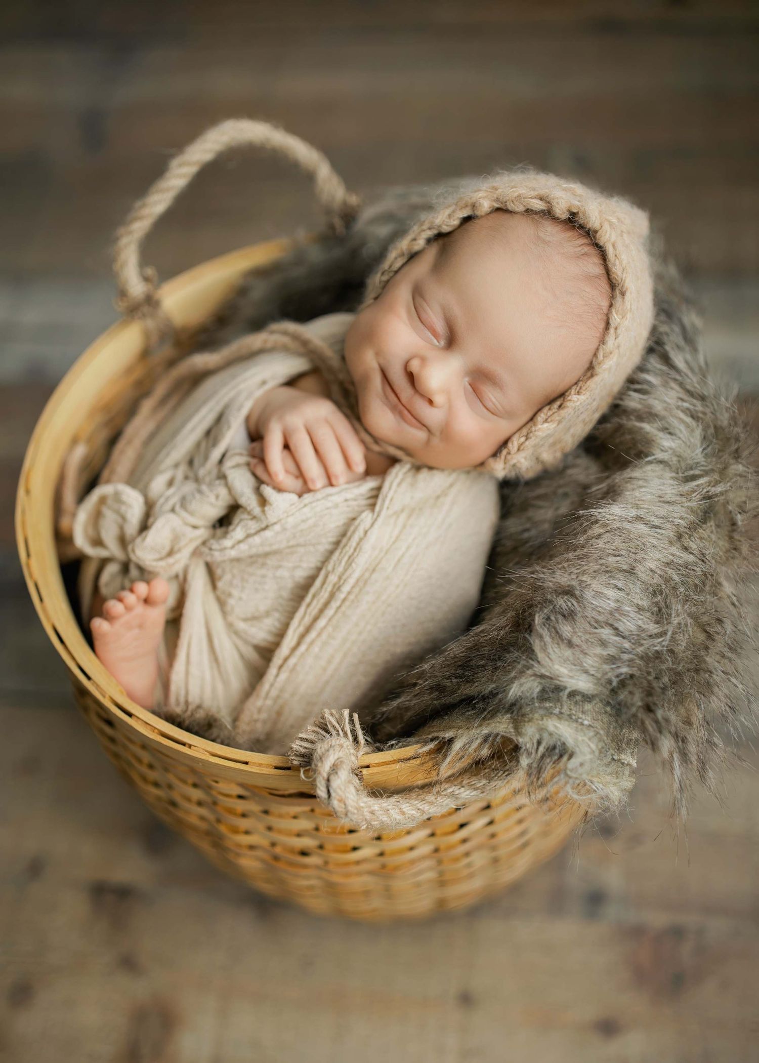Peaceful newborn sleeping in basket with cream knit wrap and soft grey fur lining.