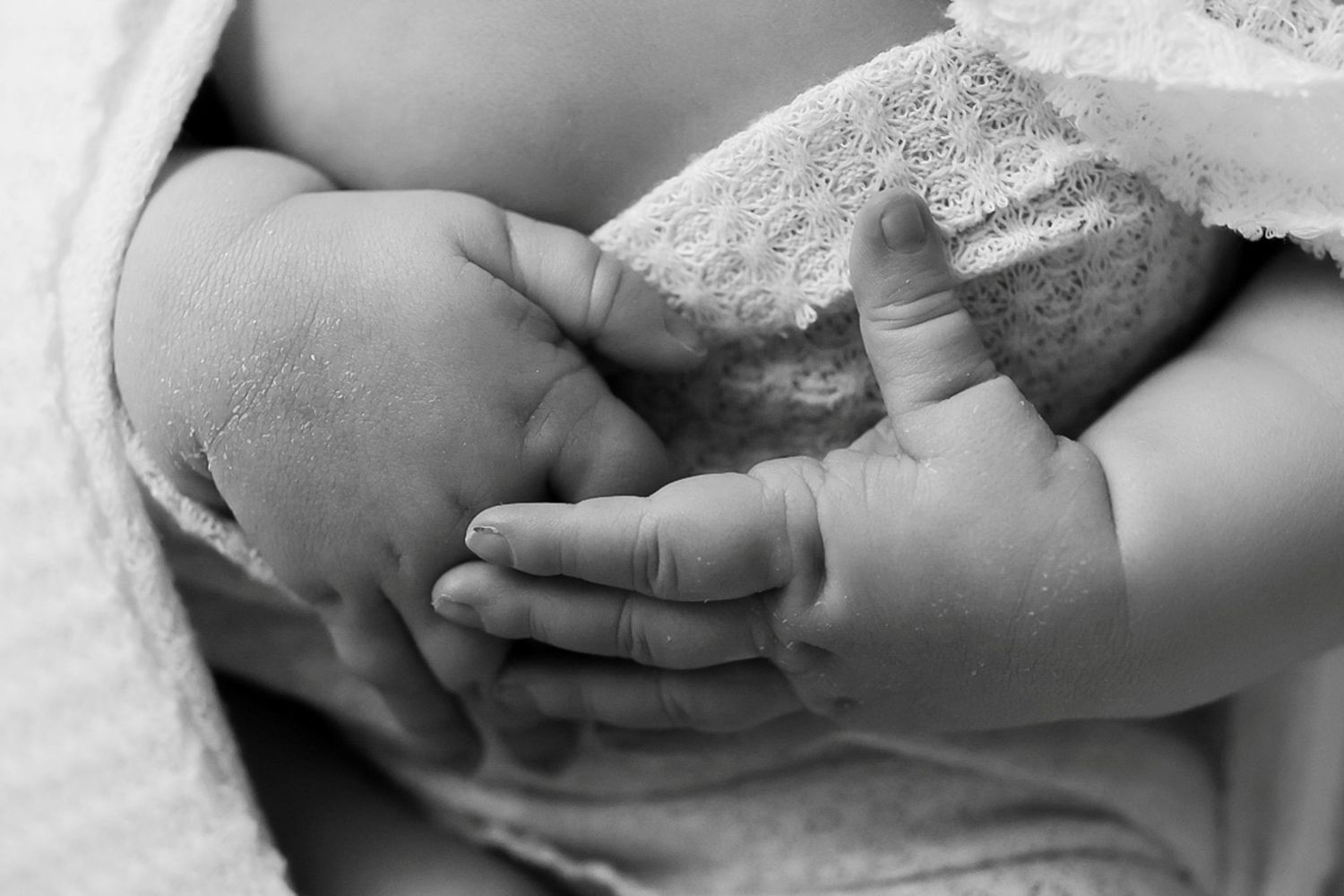 Artistic black and white detail of tiny newborn hands against white fabric.