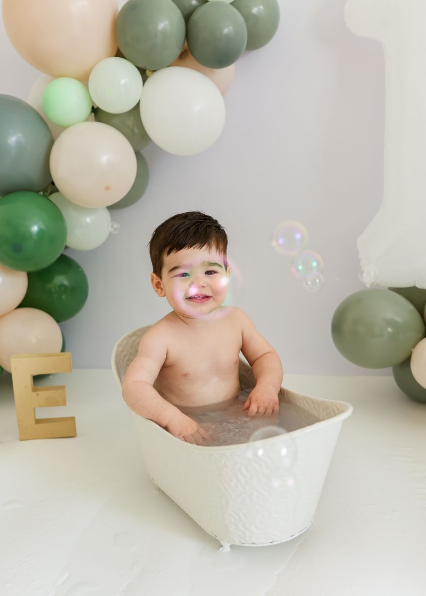 Baby bath photoshoot with green and white balloon arch and bubble decorations.