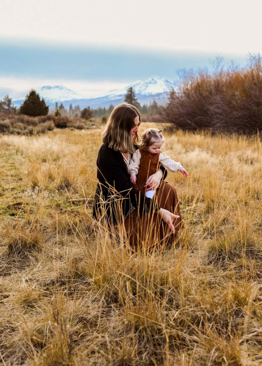 Two people sit together in golden autumn grass with snow-capped mountains visible in the distance.