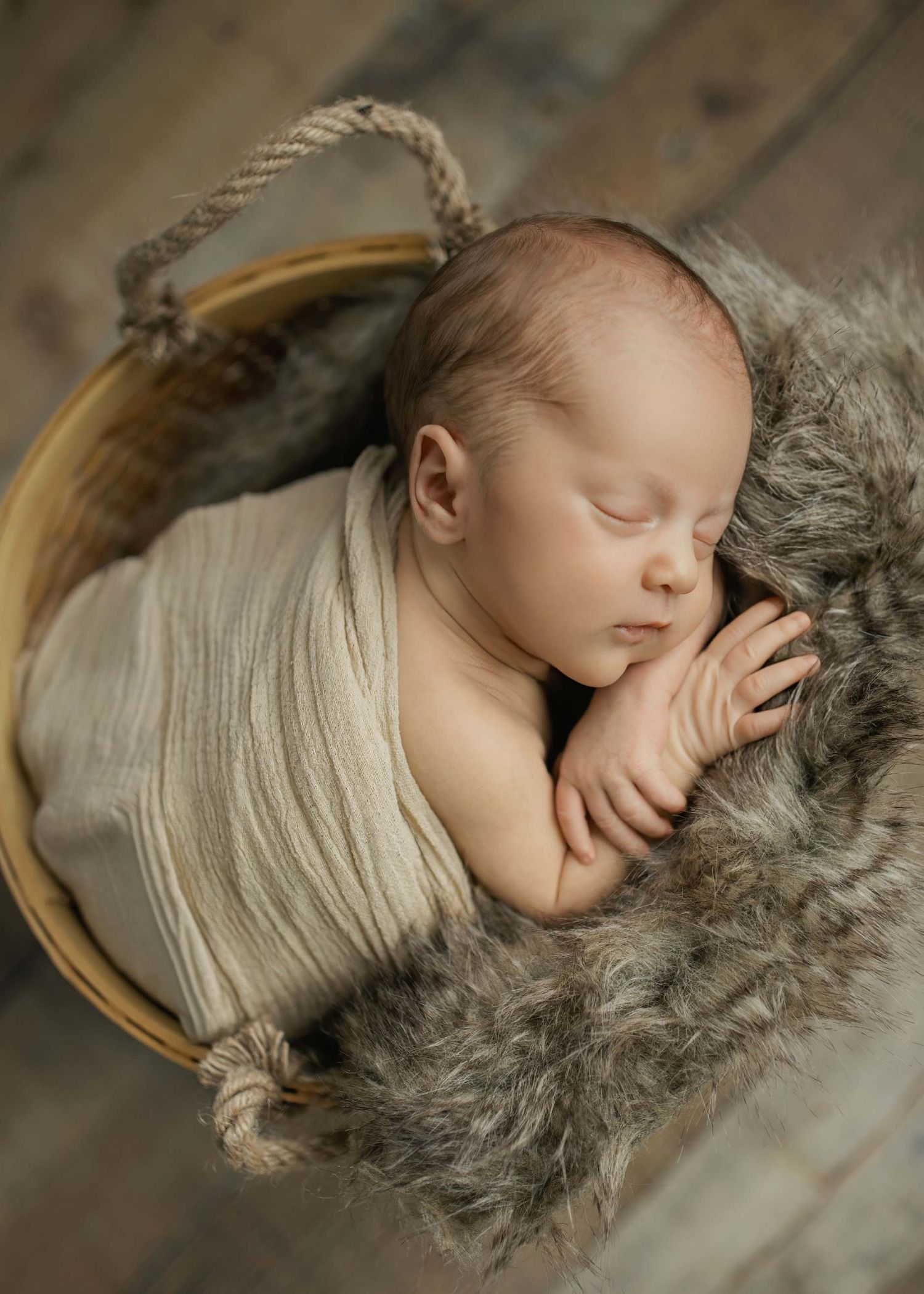 Sleeping infant nestled in woven basket with cream wrap and grey fur padding.